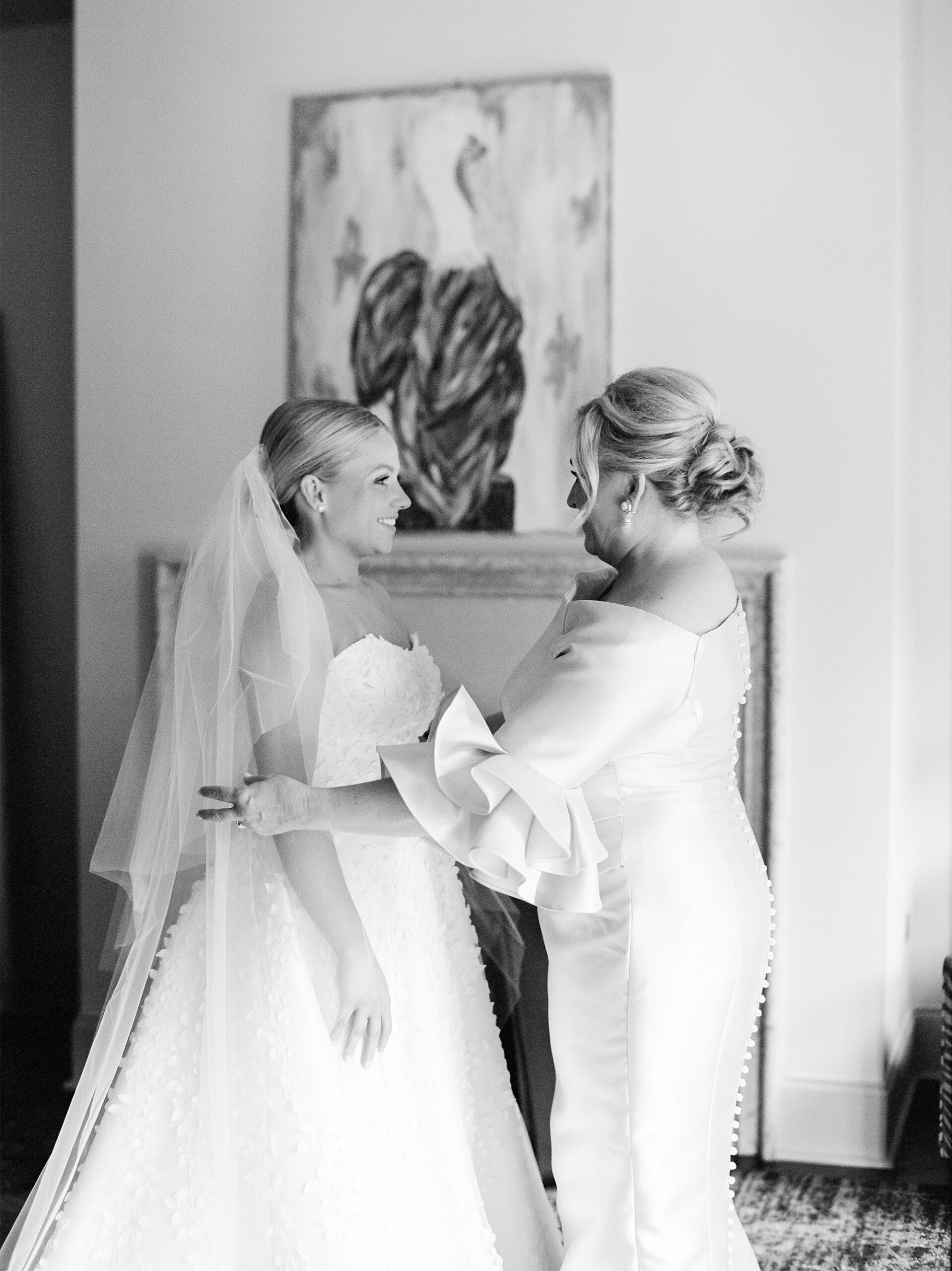 mother helps bride with wedding dress and veil 