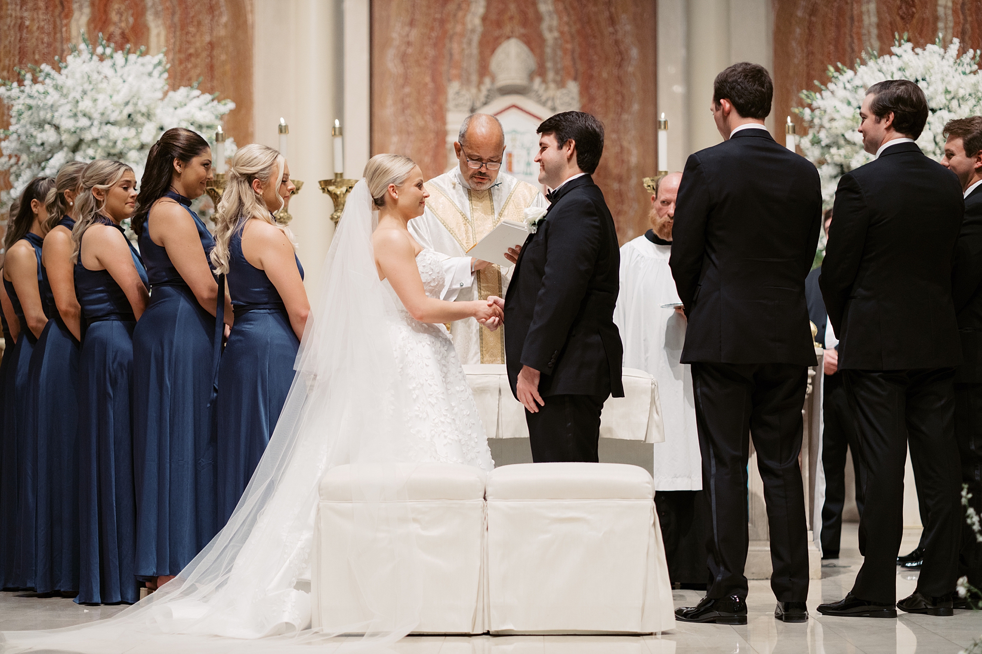 newlyweds hold hands at alter during traditional Catholic Church wedding at St. John Cathedral