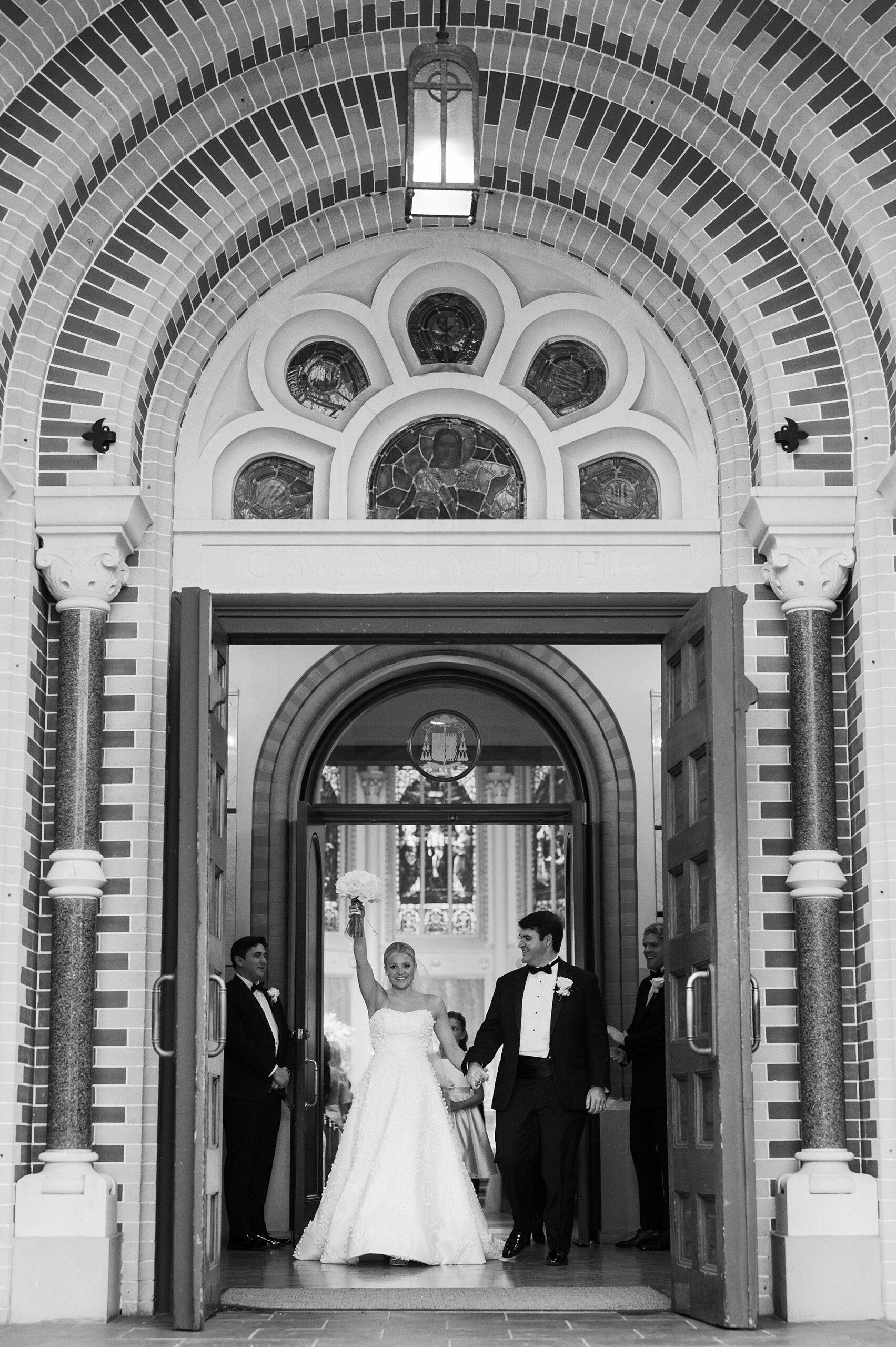 bride and groom pose on steps outside St. John Cathedral in Lafayette LA waving at guests 