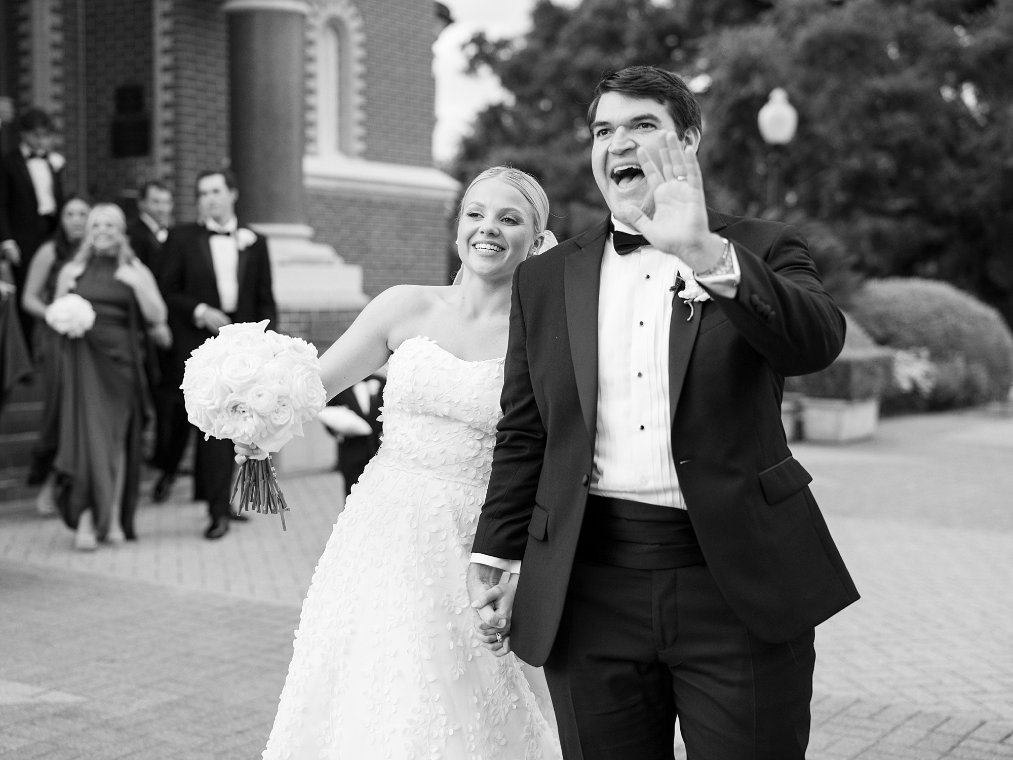 bride and groom laugh waving at guests outside St. John's Cathedral in Lafayette LA 