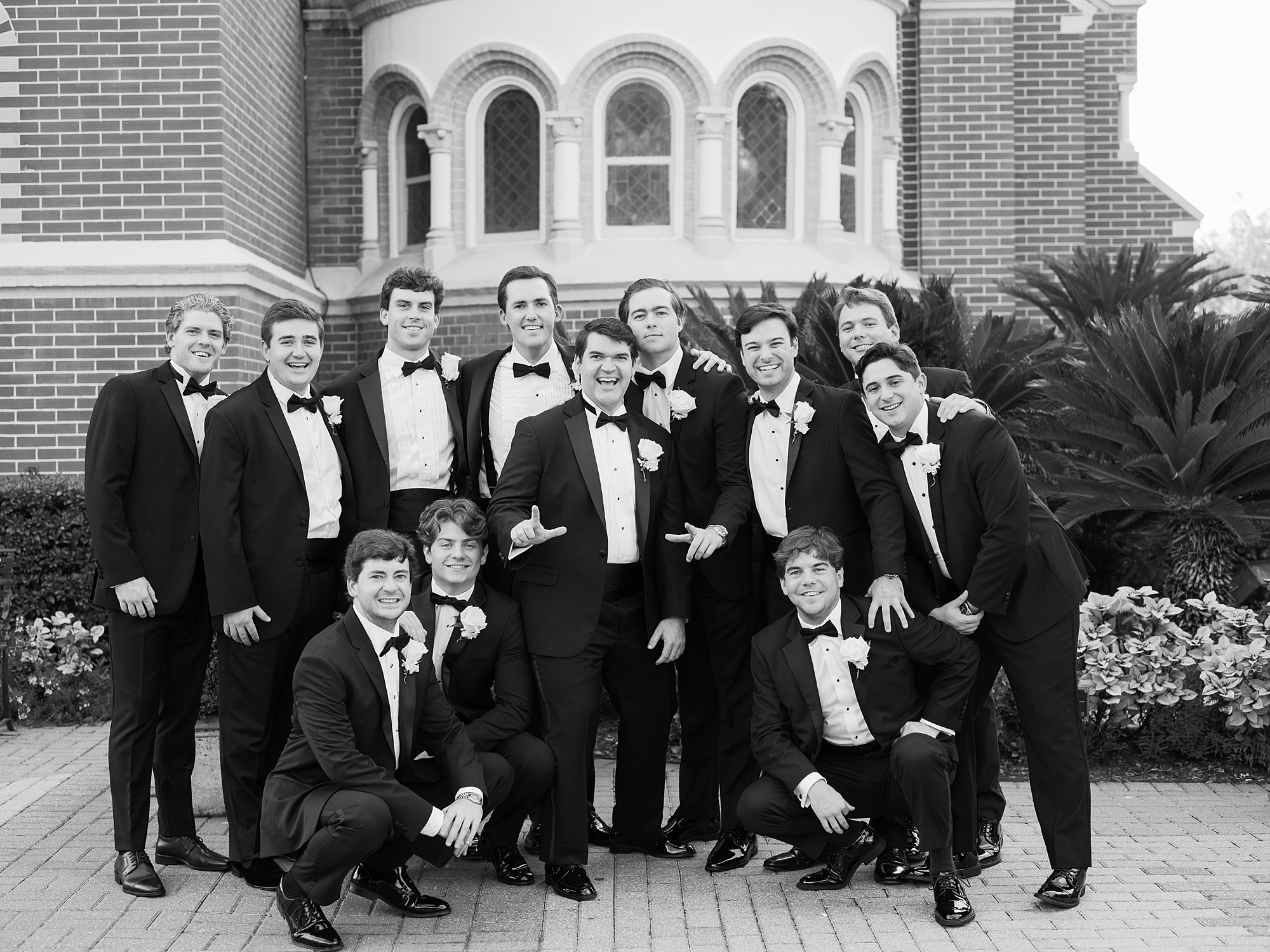 groom poses with groomsmen in black tux in front of church in Louisiana 
