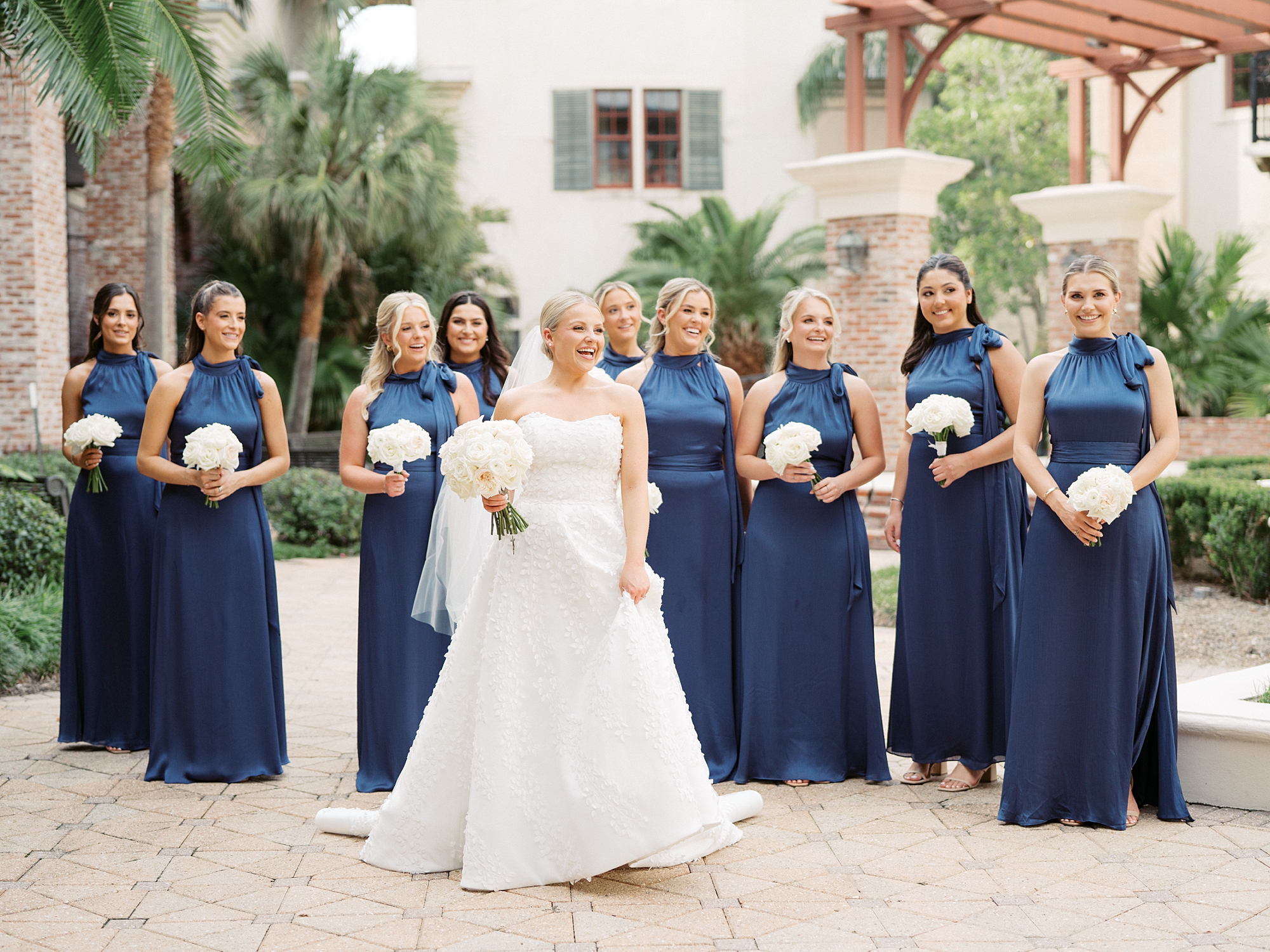 bride walks with bridesmaids in blue gowns carrying white flowers 