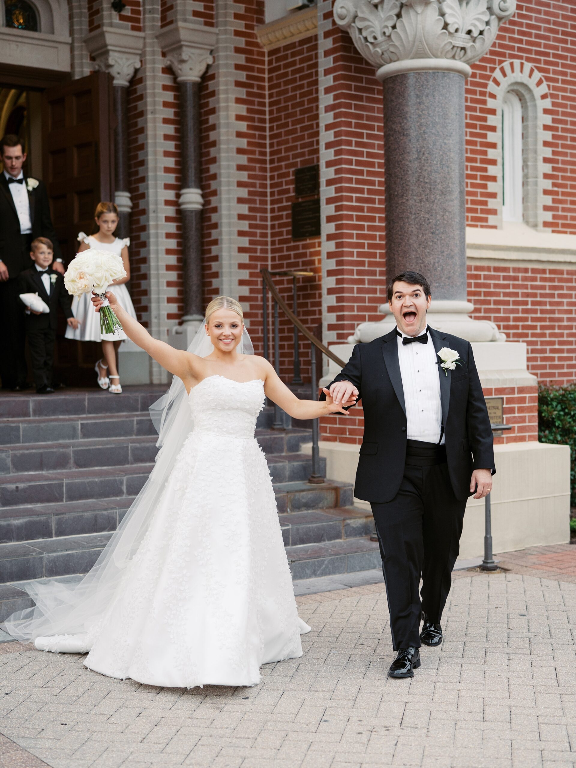 bride and groom cheer leaving traditional Catholic wedding ceremony at St. John's Cathedral