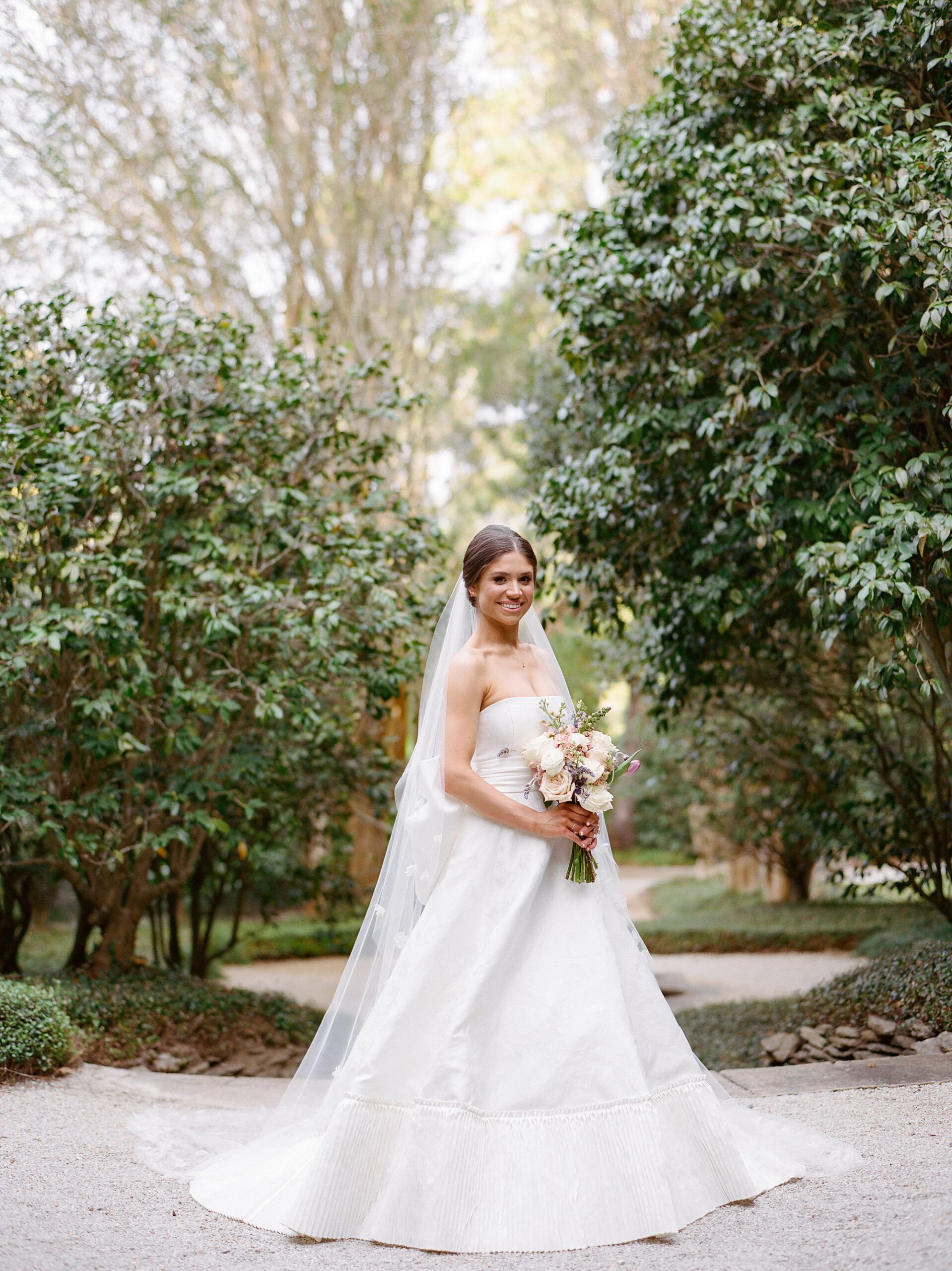 bride stands inside Rip Van Winkle gardens holding pastel bouquet