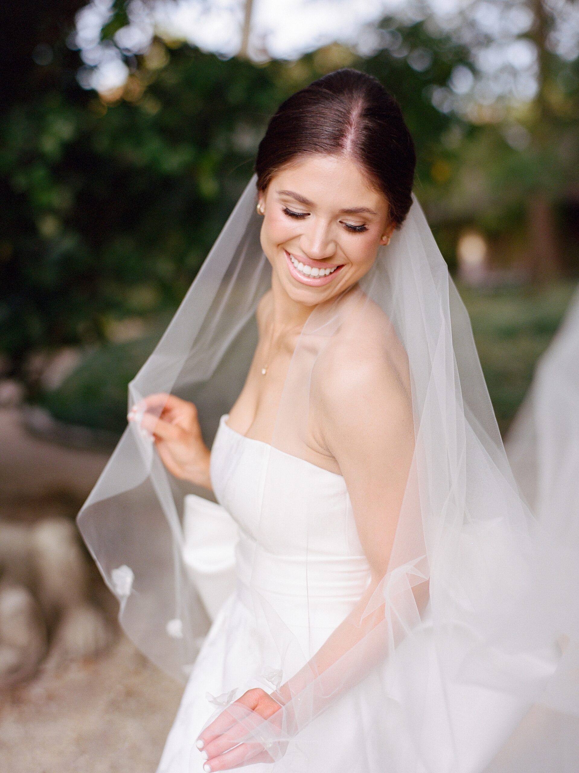 brunette bride laughs leaning with veil around her shoulders in Rip Van Winkle gardens