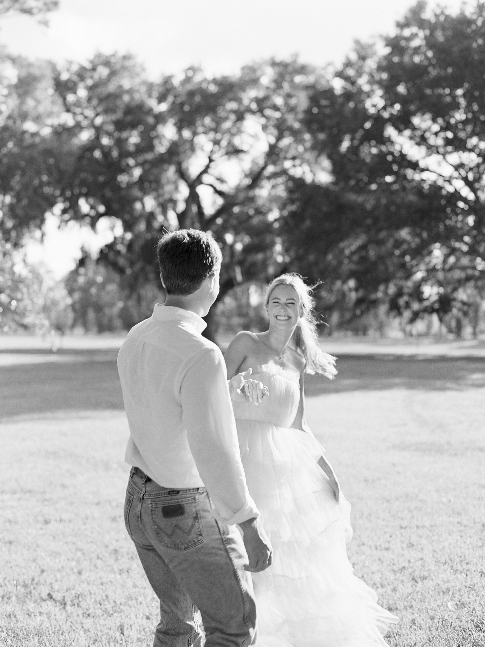 engaged couple walks on lawn dancing around during portraits at Sacred Heart of Grand Coteau
