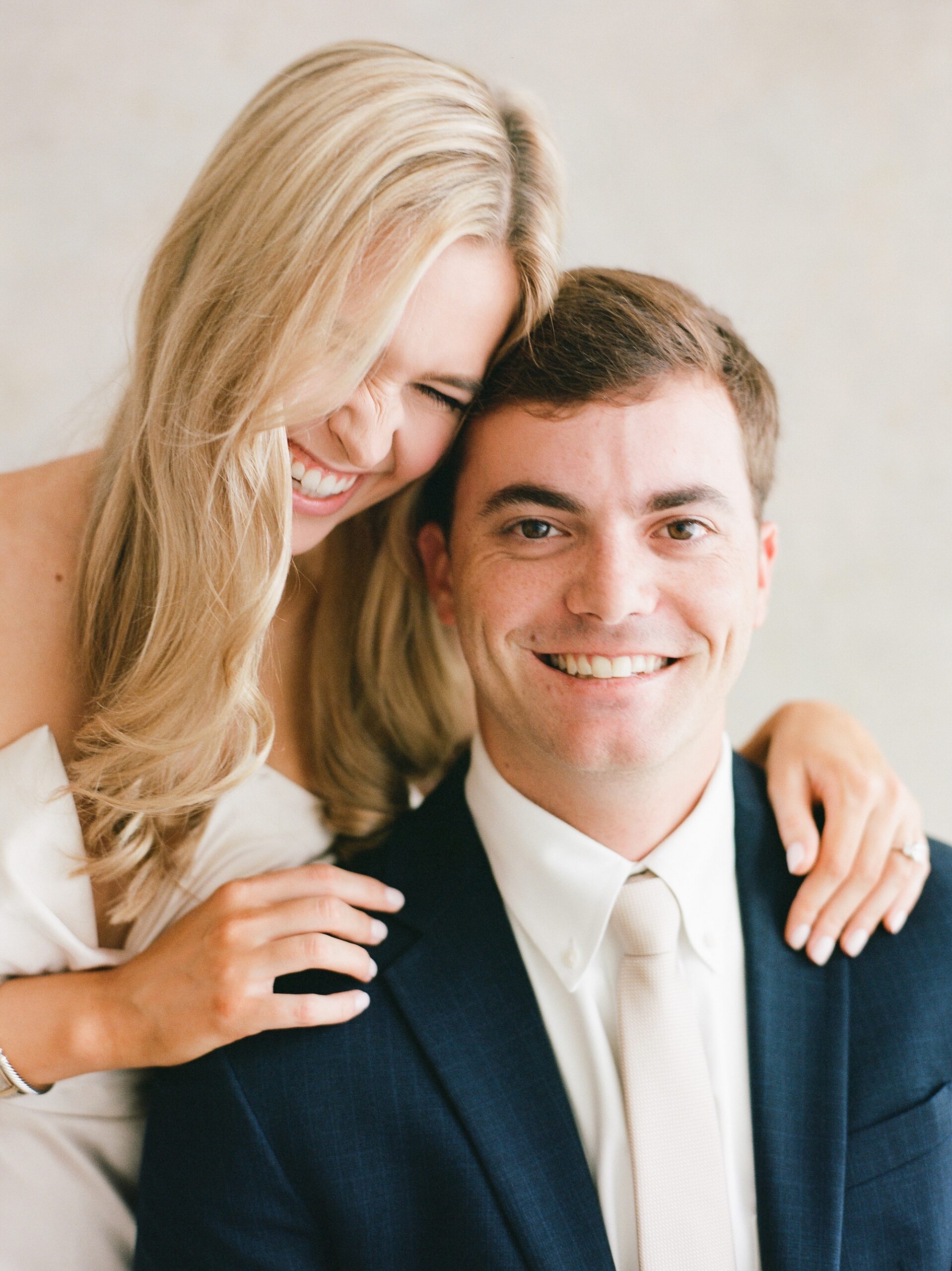 woman sits behind fiancee laughing during studio engagement portraits in Louisiana 