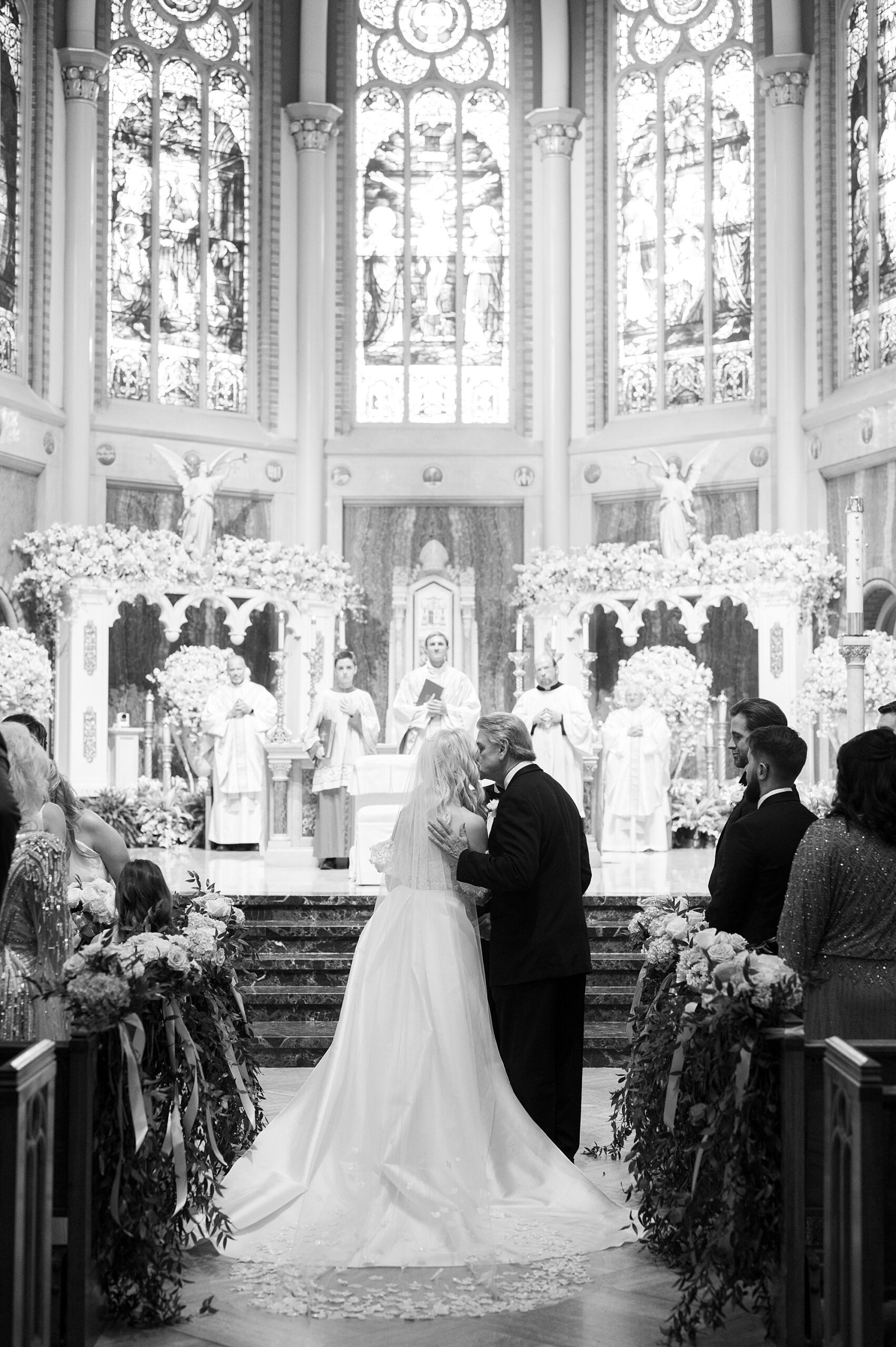 father kisses bride on cheek walking up aisle in church in Lafayette LA
