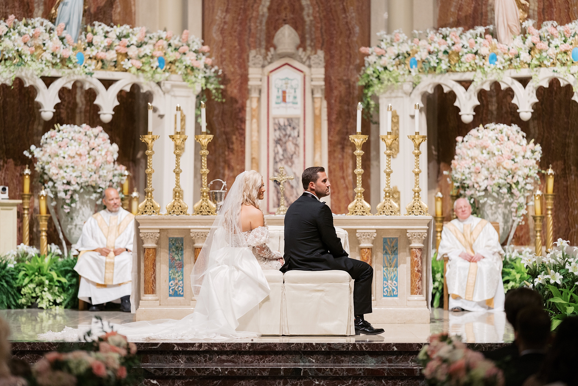 bride and groom sit inside Cathedral Of St. John during traditional Catholic wedding ceremony