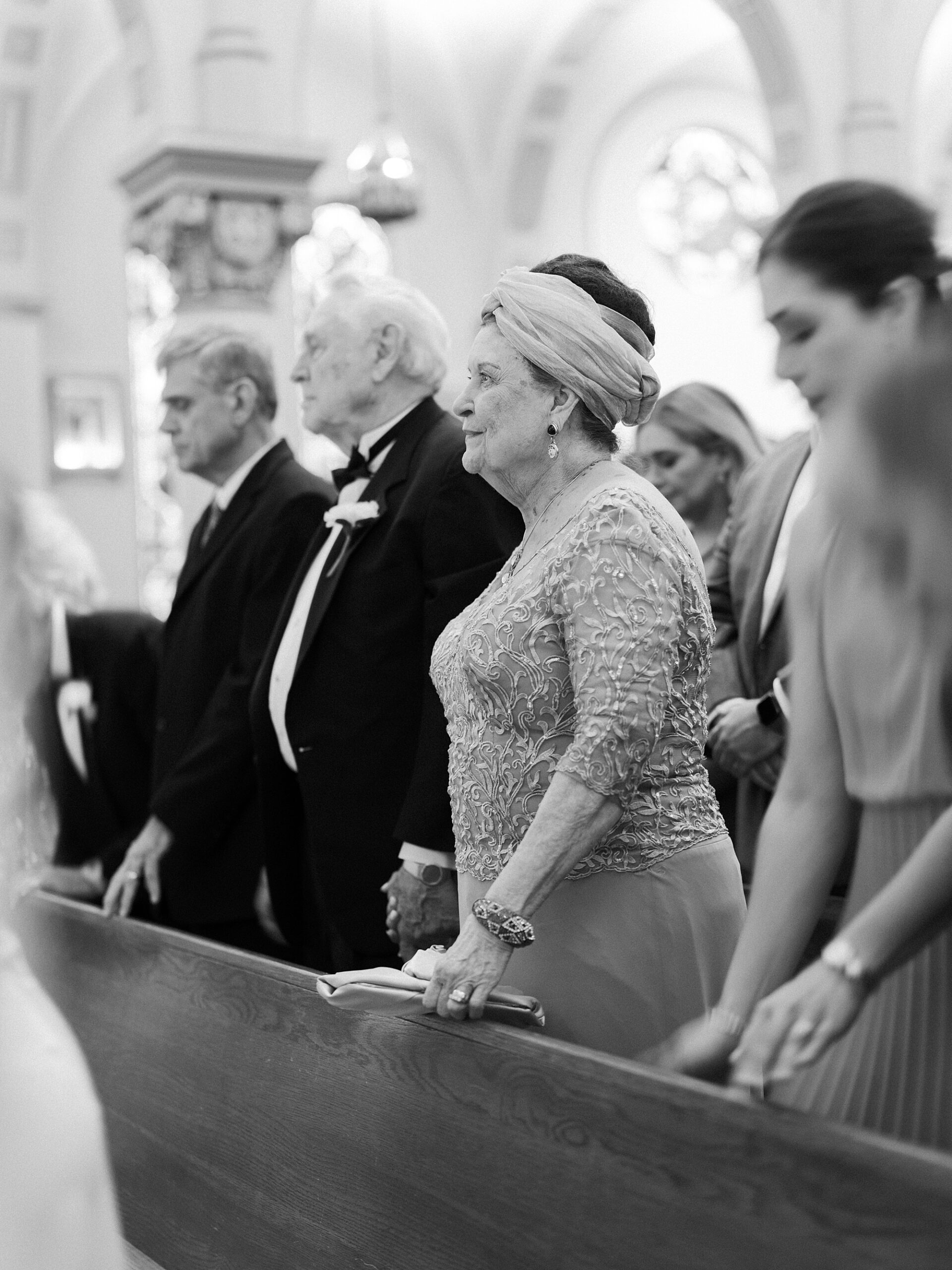 family stands in pews during Cathedral Of St. John during traditional Catholic wedding ceremony