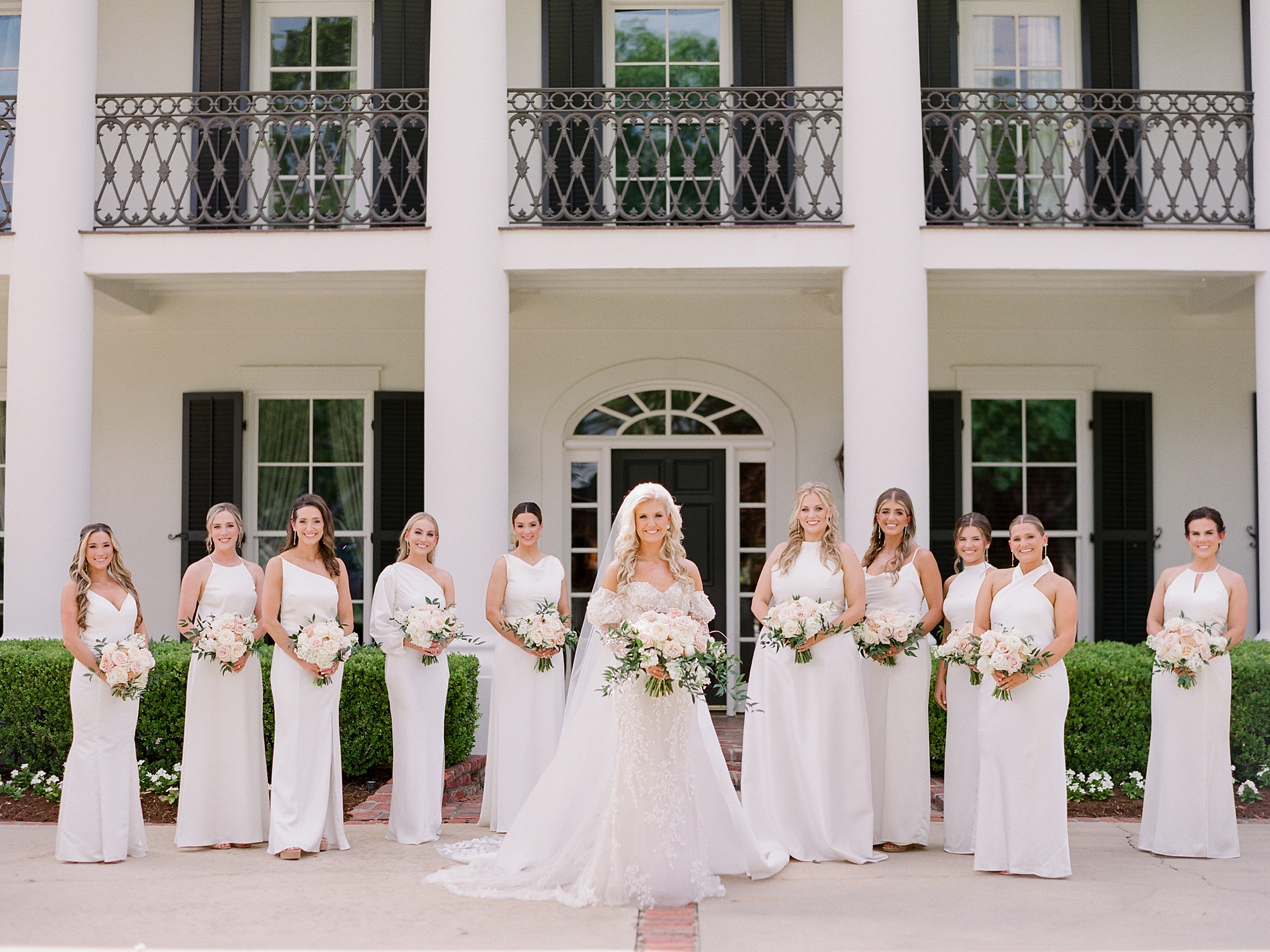 bride stands in front of bridesmaids in ivory gowns outside the University of Louisiana at Lafayette alumni center