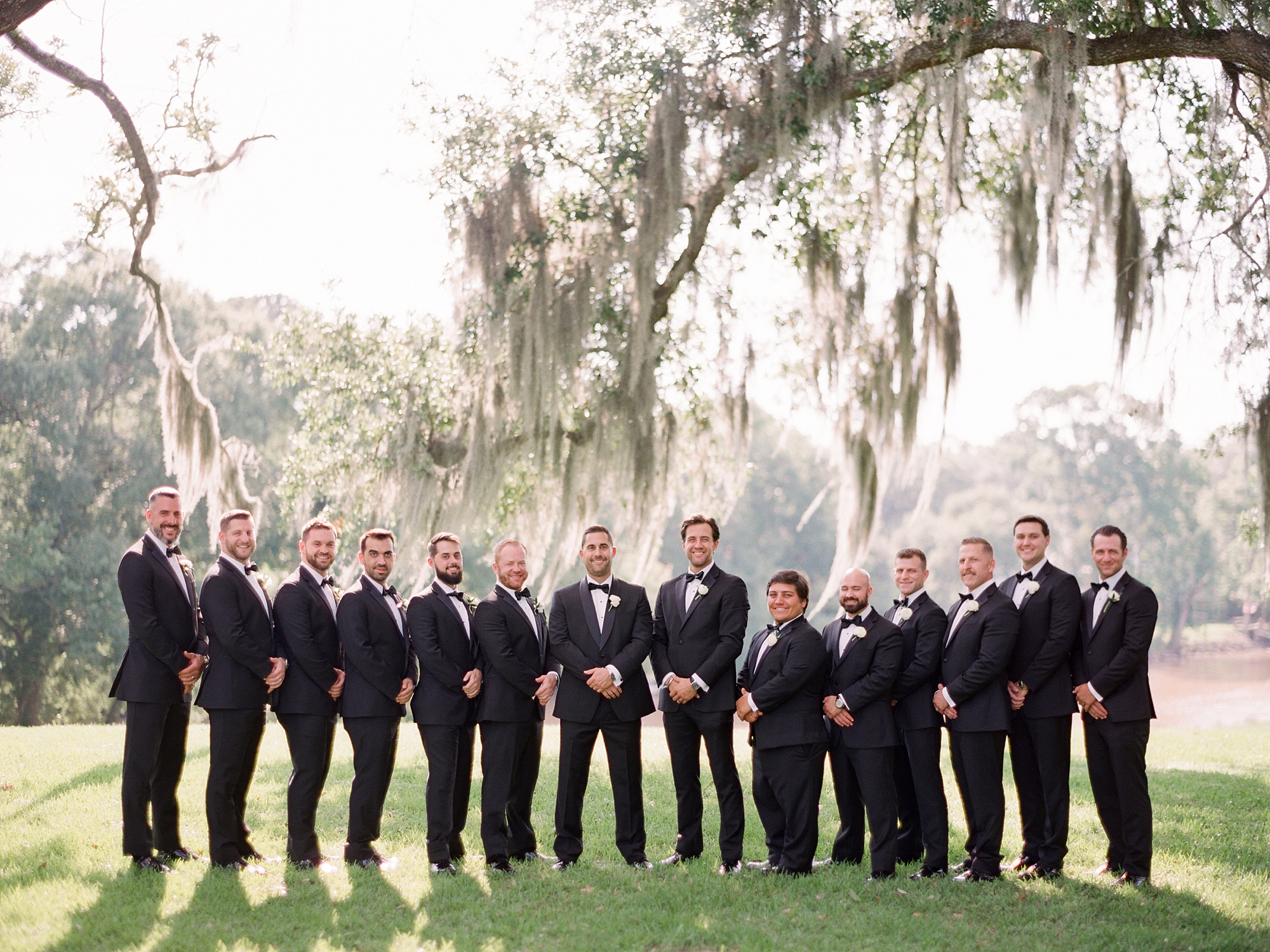 groom stands with groomsmen in black suits under tree with Spanish moss at the University of Louisiana at Lafayette alumni center
