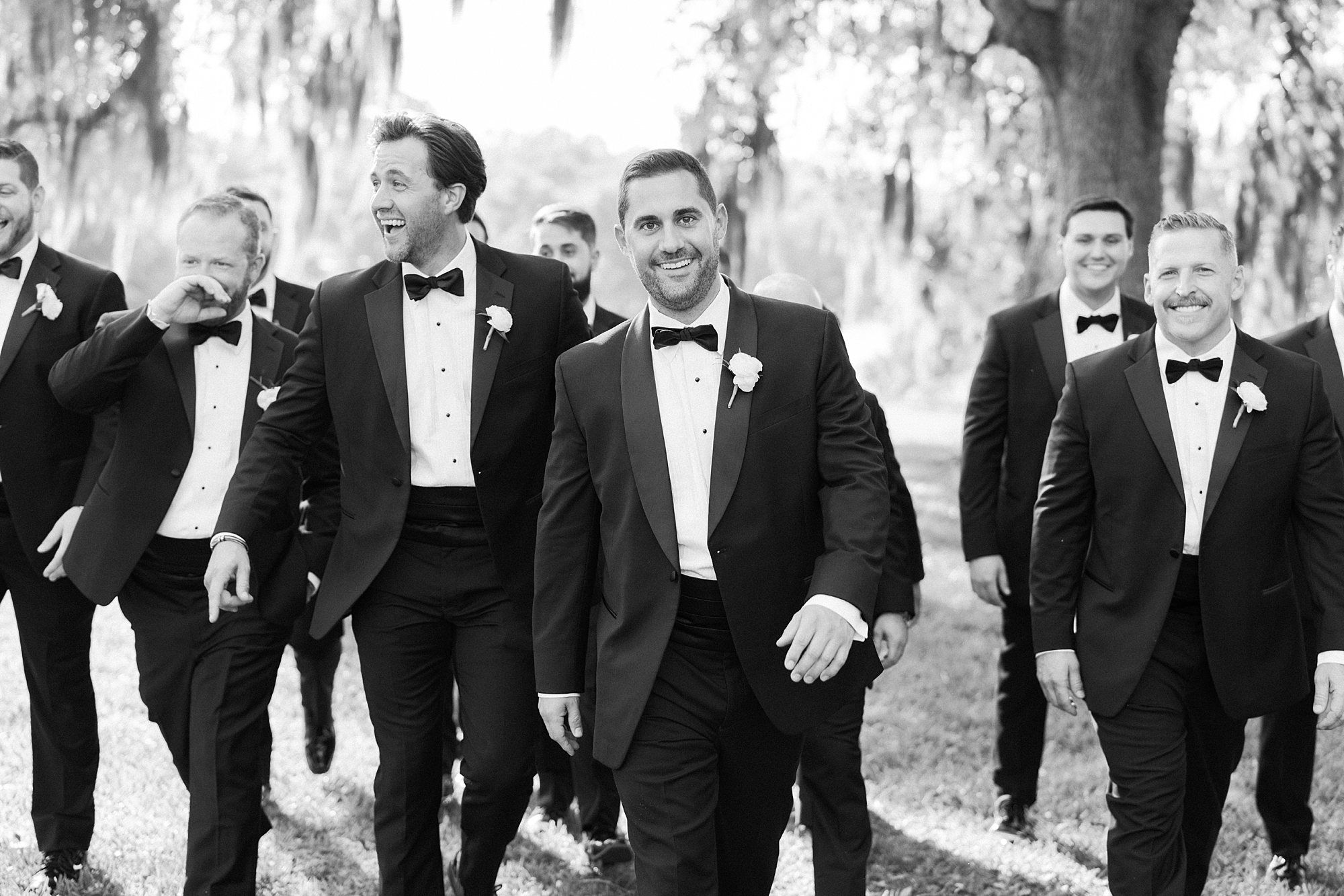 groom in black tux walks with groomsmen under Spanish moss at the University of Louisiana at Lafayette alumni center