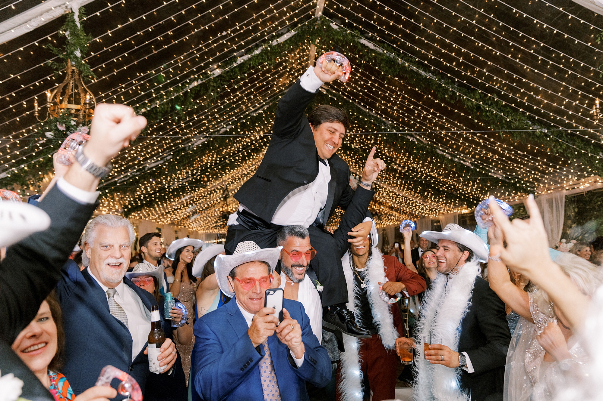 guests lift up groom during wedding reception under tent