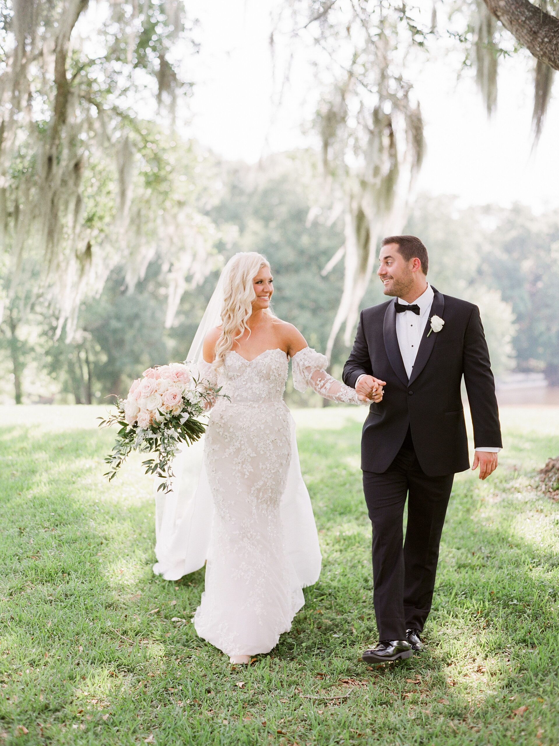 bride and groom link arms walking under Spanish moss outside the University of Louisiana at Lafayette alumni center