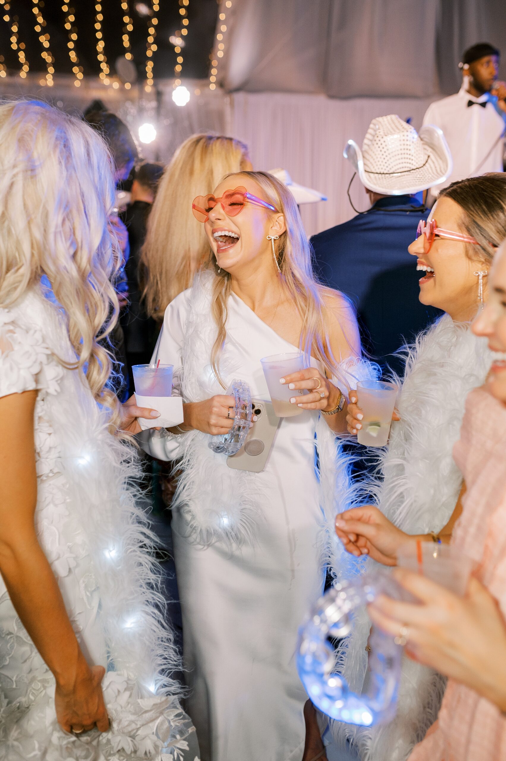 bride laughs with guests in pink heart glasses and white dress 