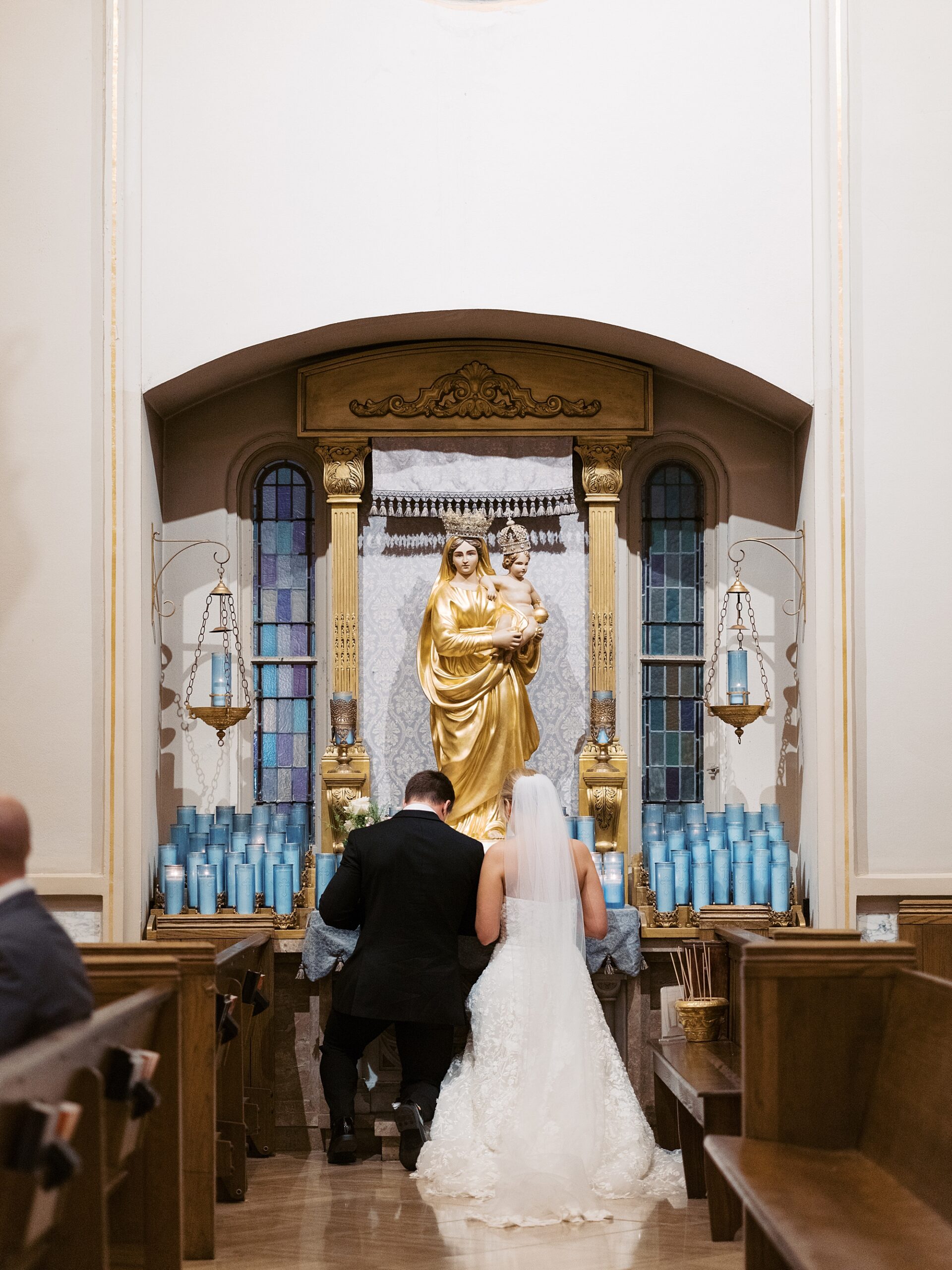 bride and groom pray at statue of Mary inside the Cathedral of St. John the Evangelist
