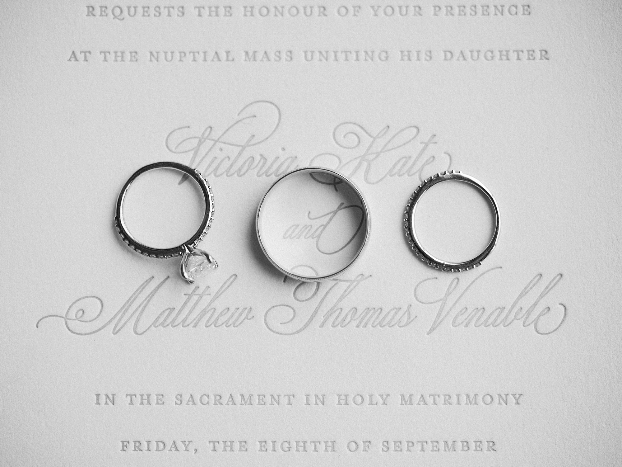 three wedding bands lay on scripted wedding invitation 