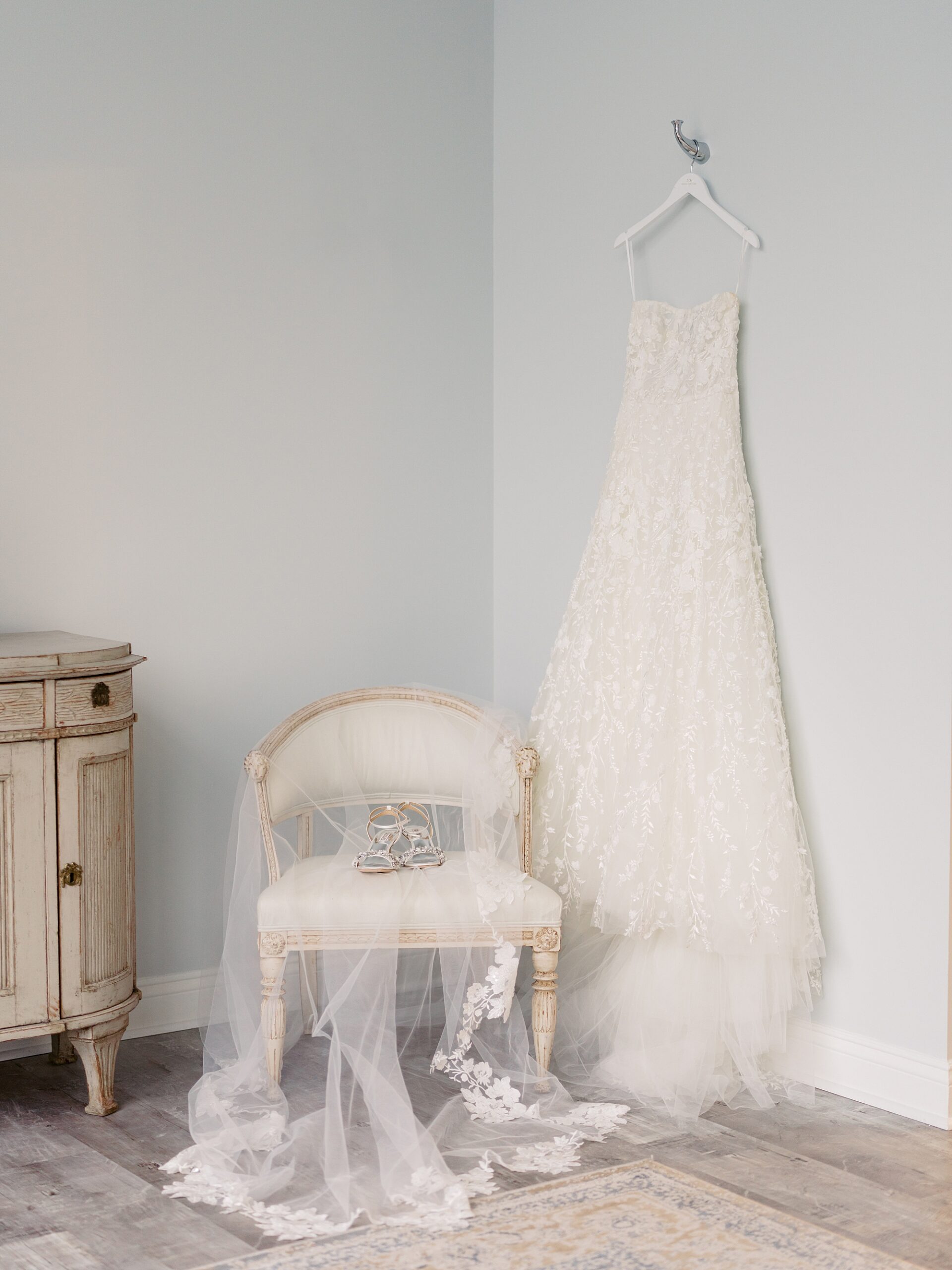 wedding dress hangs in corner of room with veil on chair at Le Pavilion Hotel