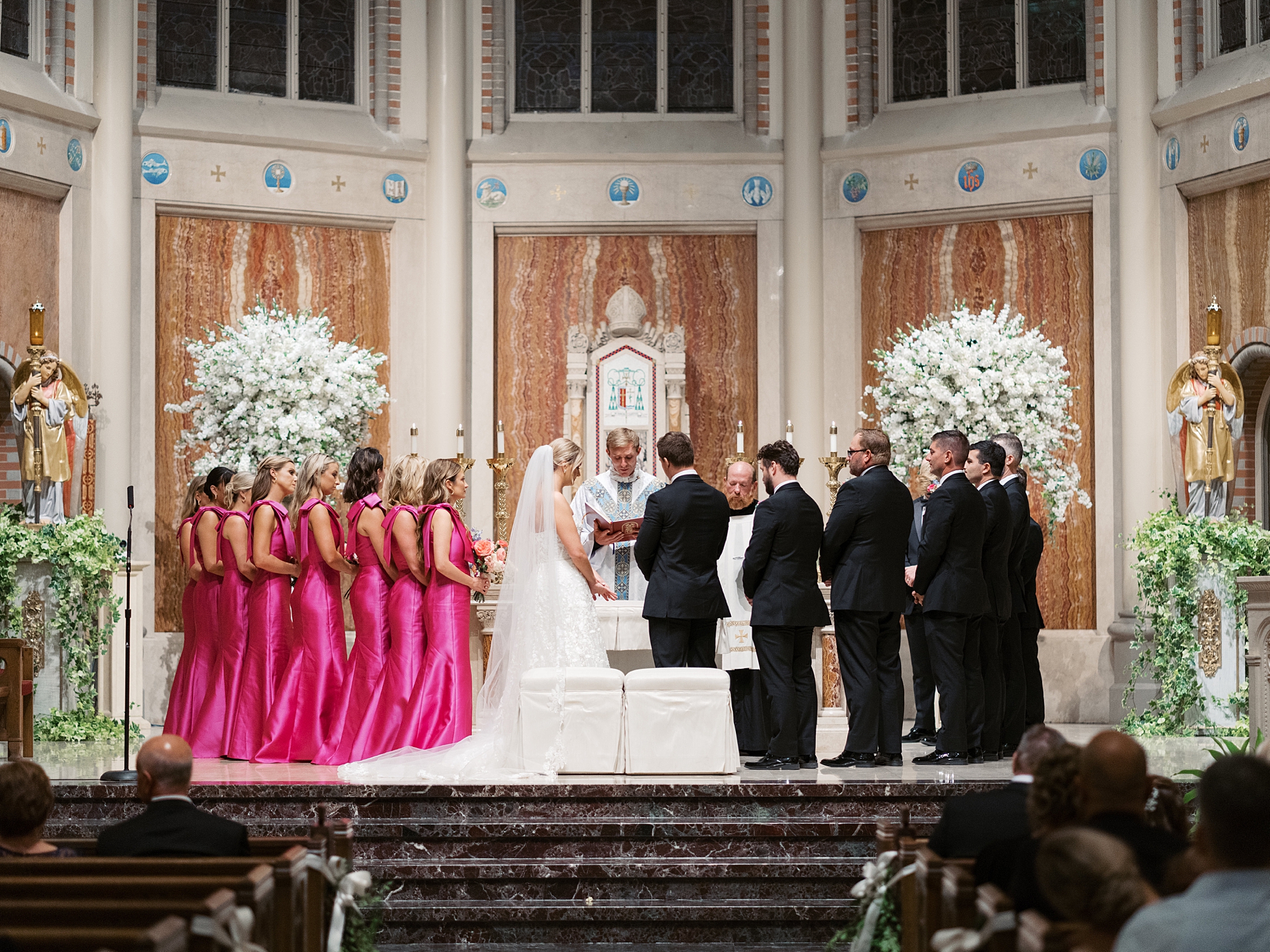 bride and groom stand at alter inside Cathedral of St. John the Evangelist with wedding party in pink gowns and black tuxes 