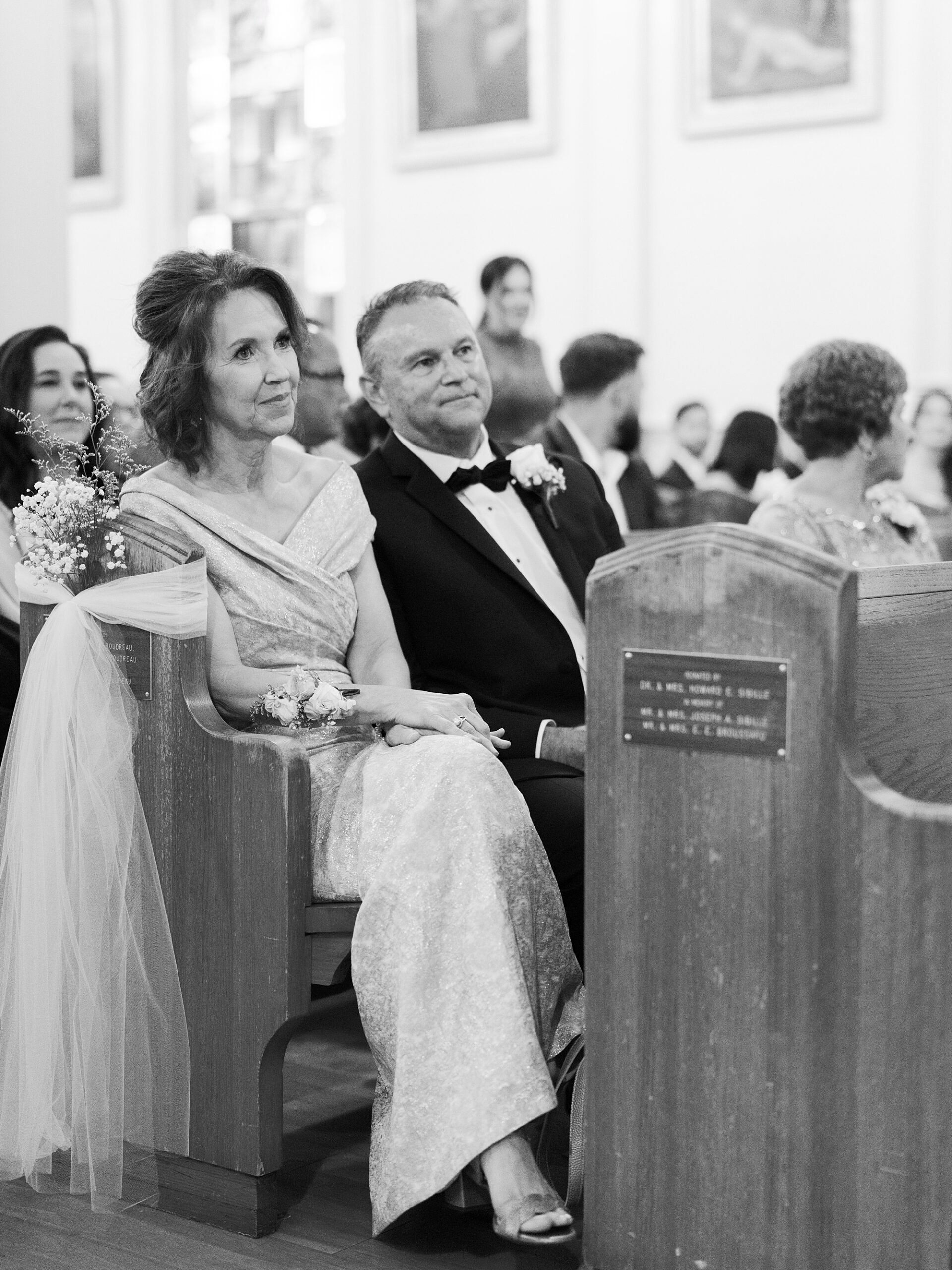 mother and father watch from pew during traditional catholic wedding ceremony inside St. Charles Borromeo