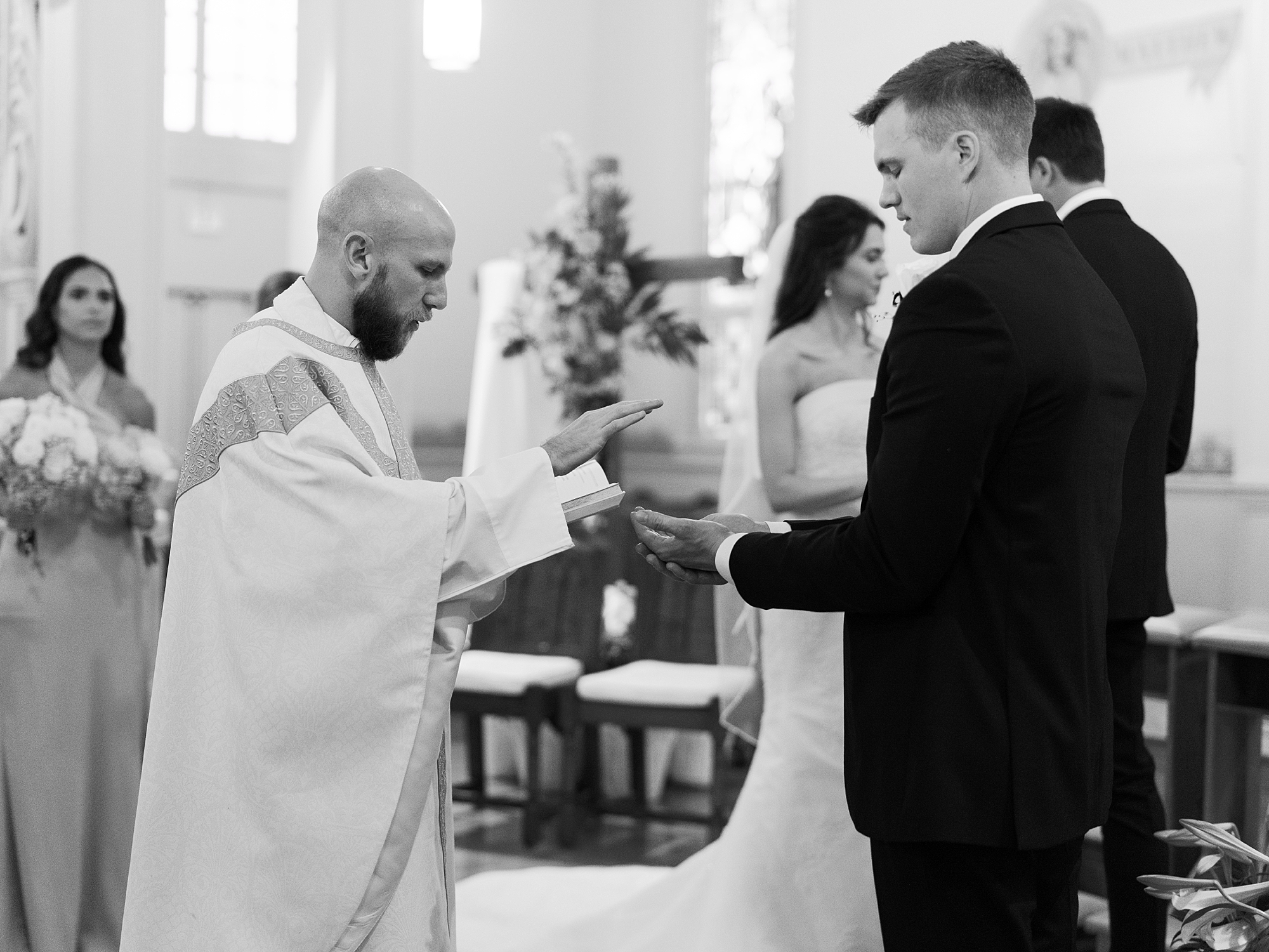 father gives rings to groom during traditional catholic wedding ceremony inside St. Charles Borromeo