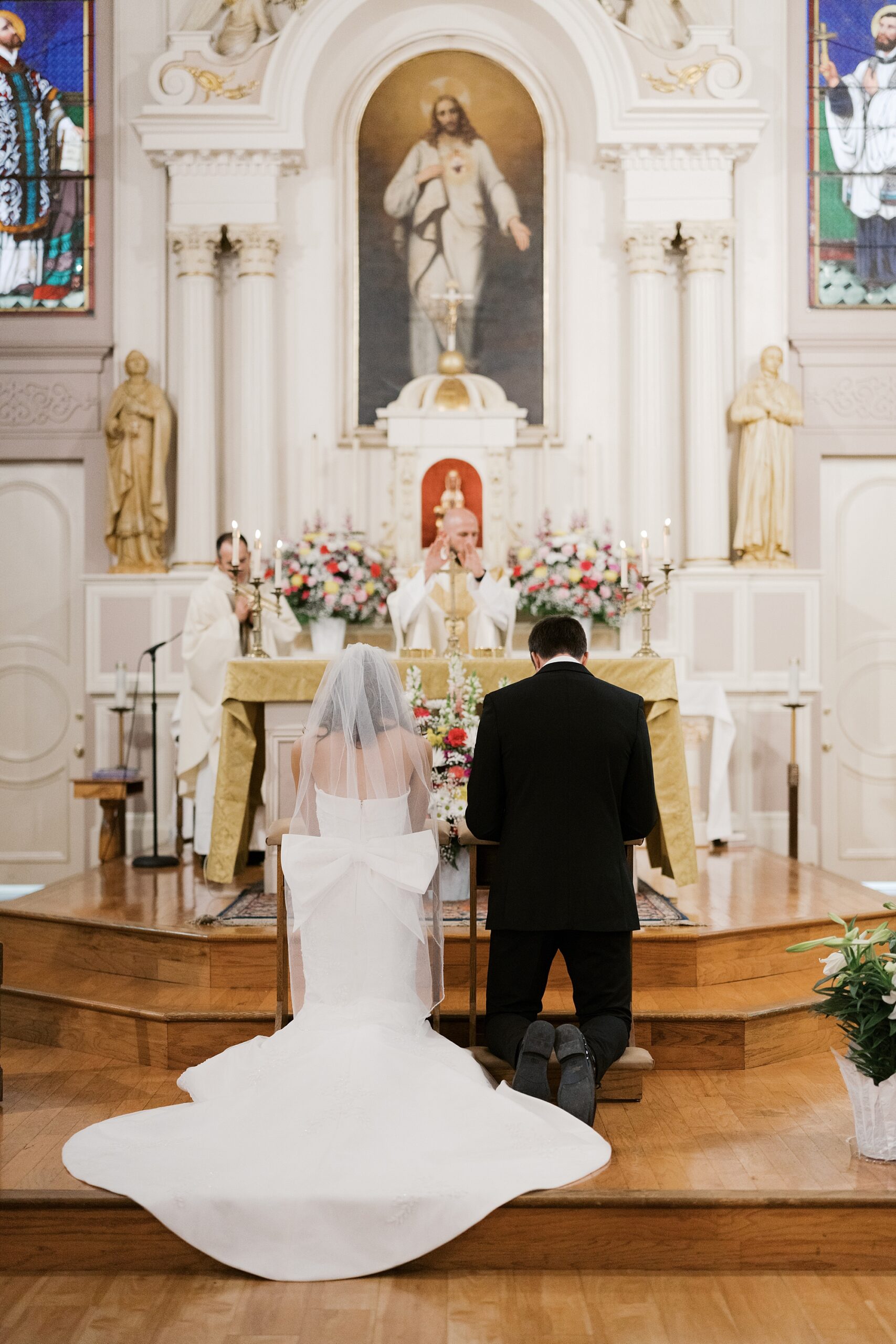 bride and groom kneel at alter during traditional catholic wedding ceremony inside St. Charles Borromeo