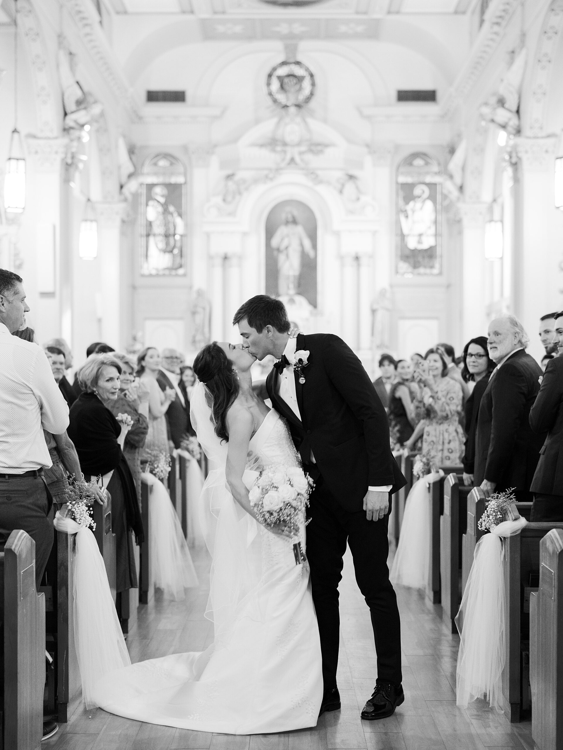 newlyweds kiss in aisle after traditional catholic wedding ceremony inside St. Charles Borromeo