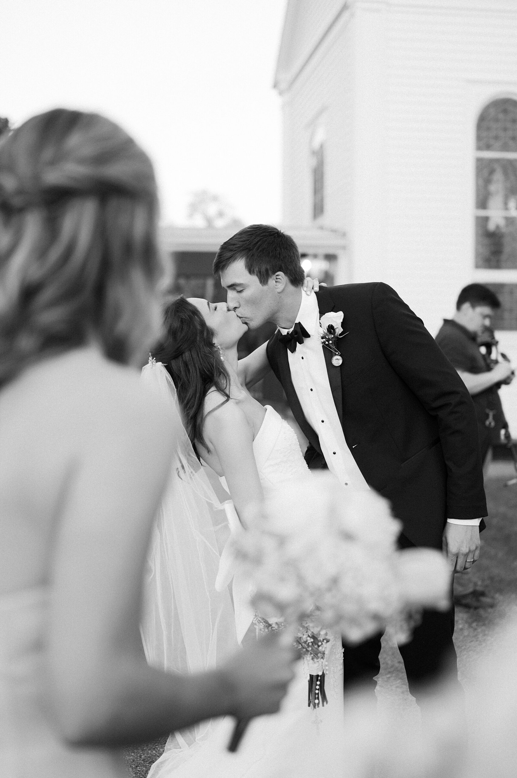 groom leans to kiss bride during portraits outside St. Charles Borromeo