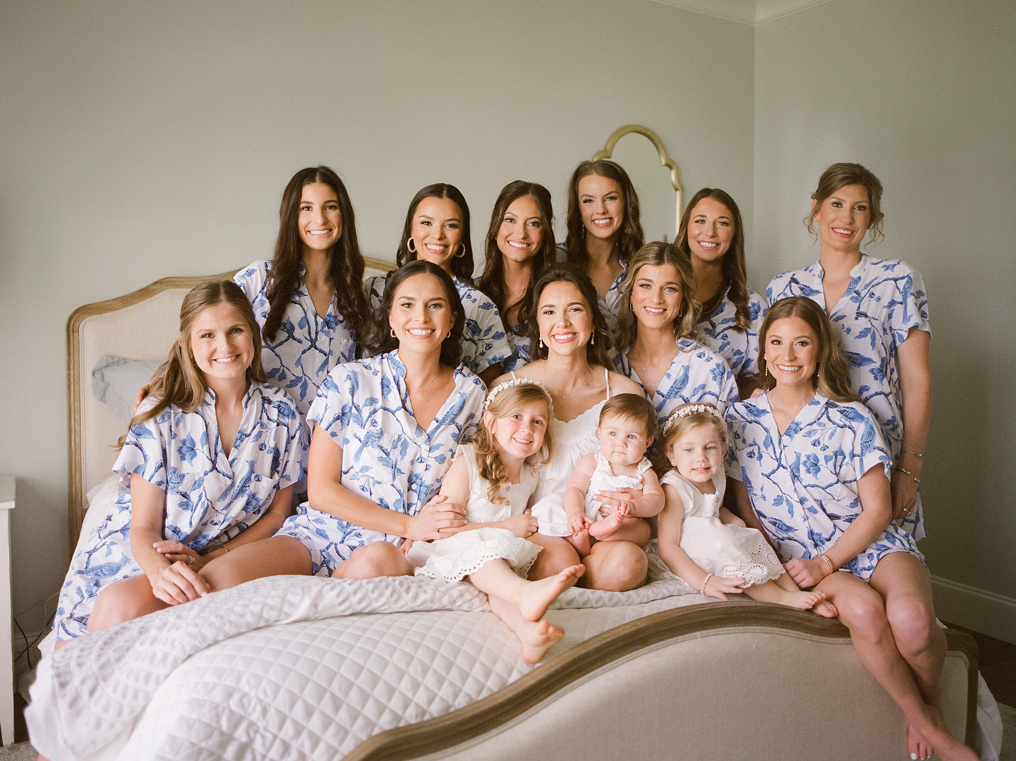 bride poses on bed with bridesmaids and flower girls