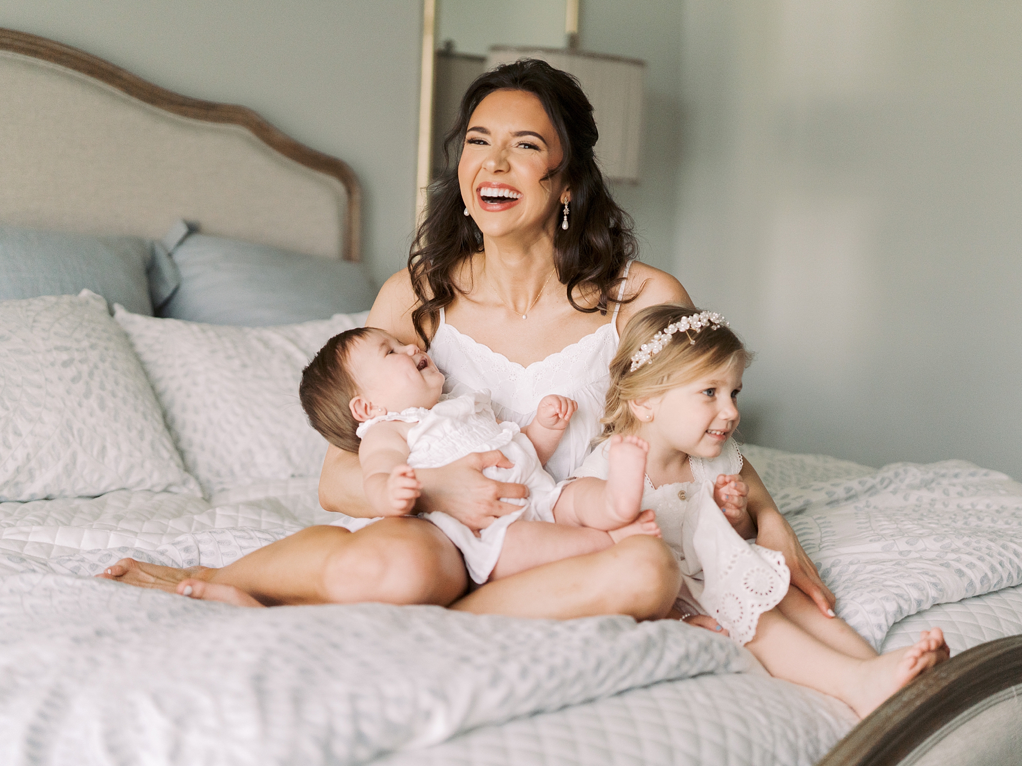 bride poses on bed with two younger flower girls