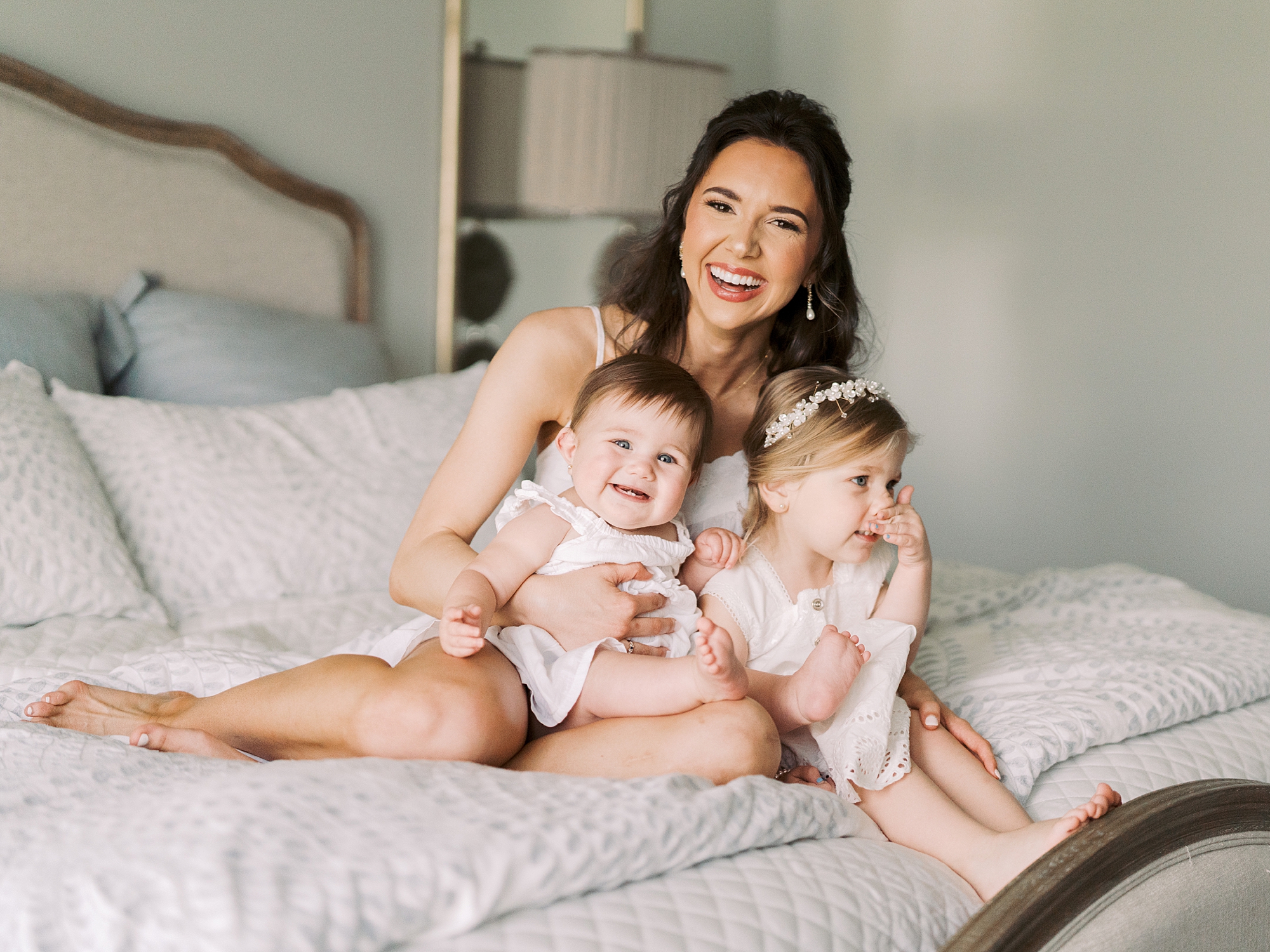 bride poses on bed with two younger flower girls