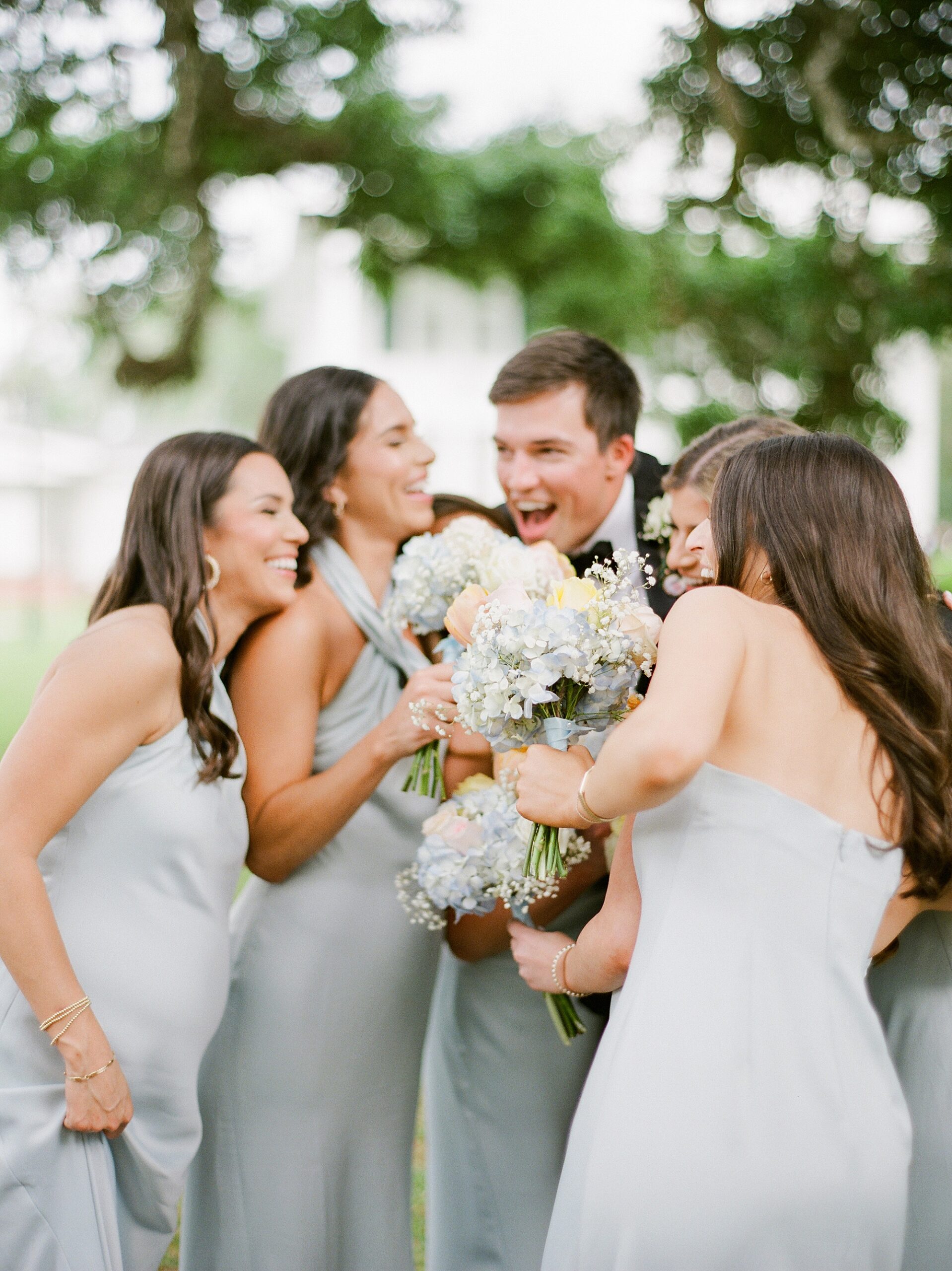 groom laughs with bridesmaids outside Oakbourne Country Club