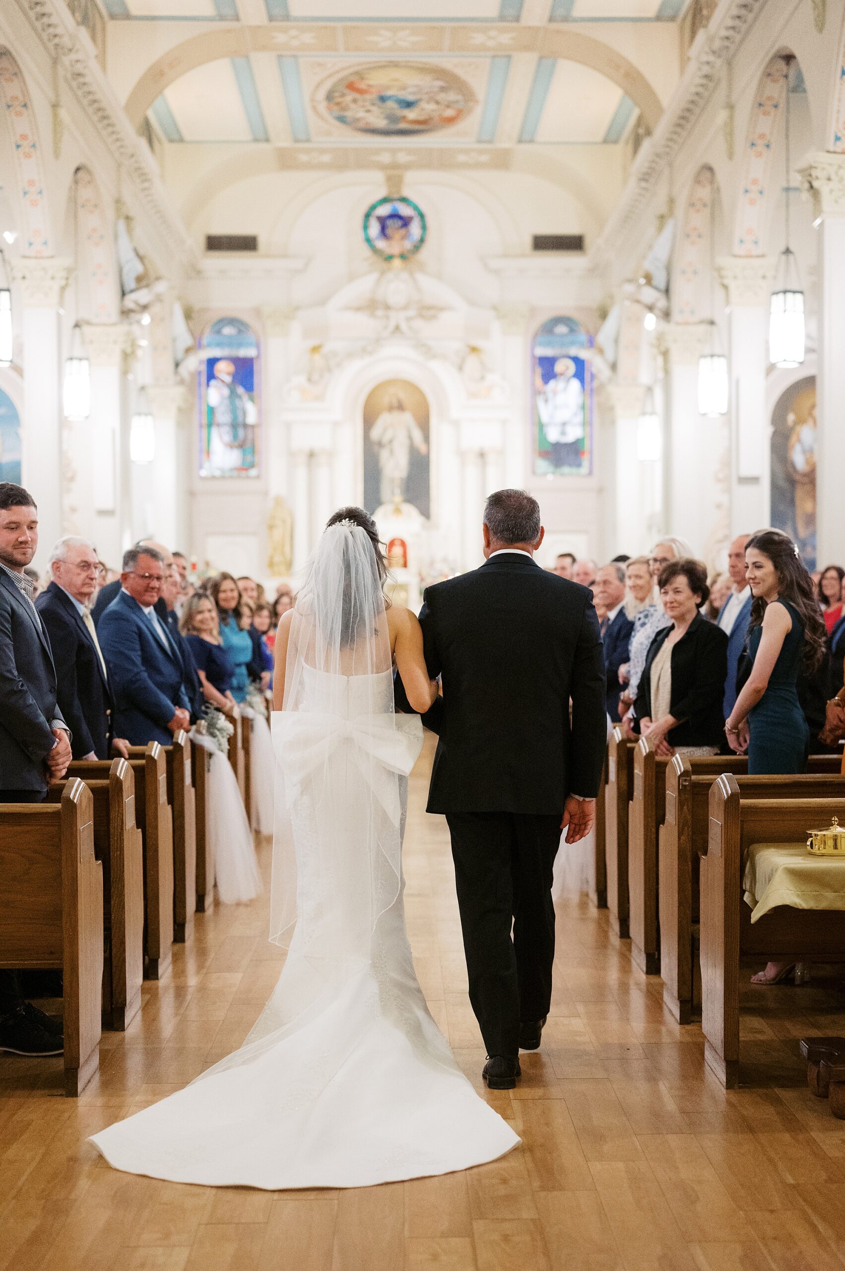 bride walks down aisle with father during traditional catholic wedding ceremony inside St. Charles Borromeo