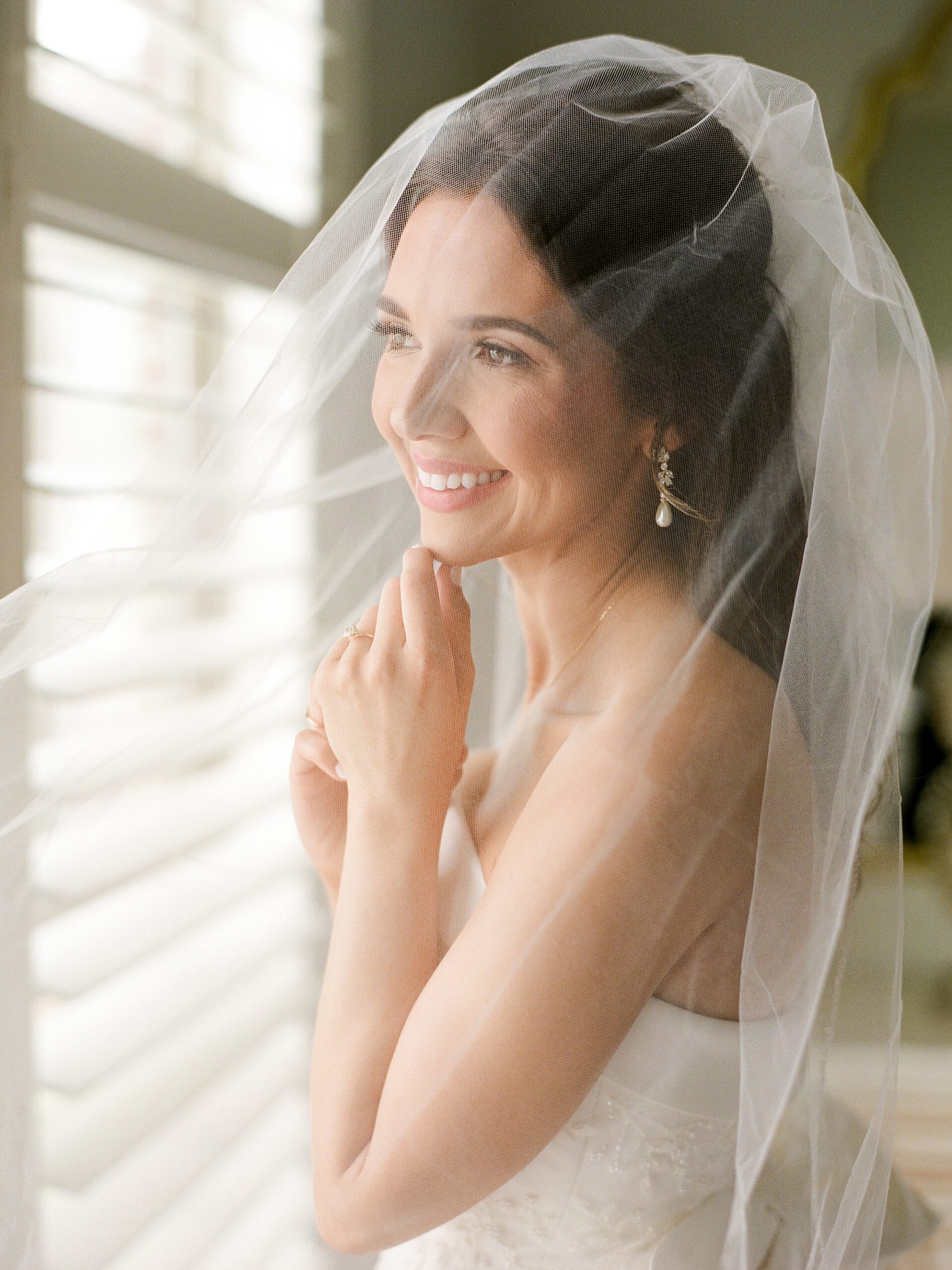 bride looks out window with veil over face 