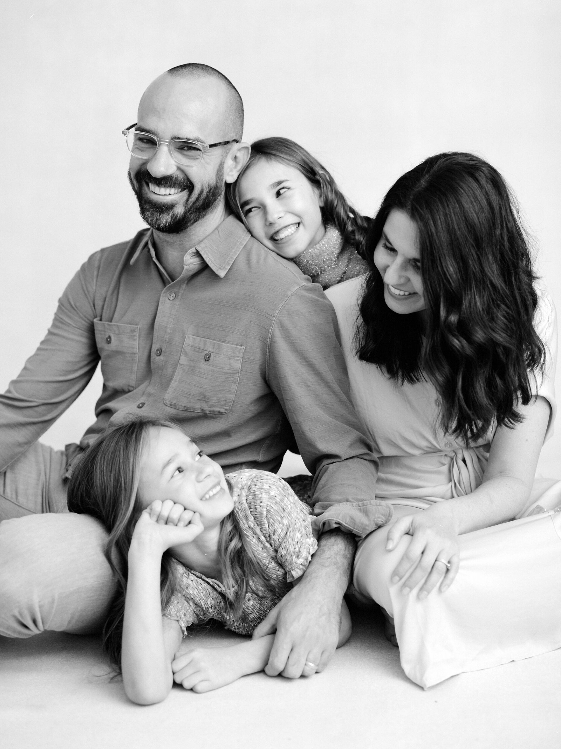 parents smile with two daughters laying on them during studio family photos in Lafayette LA