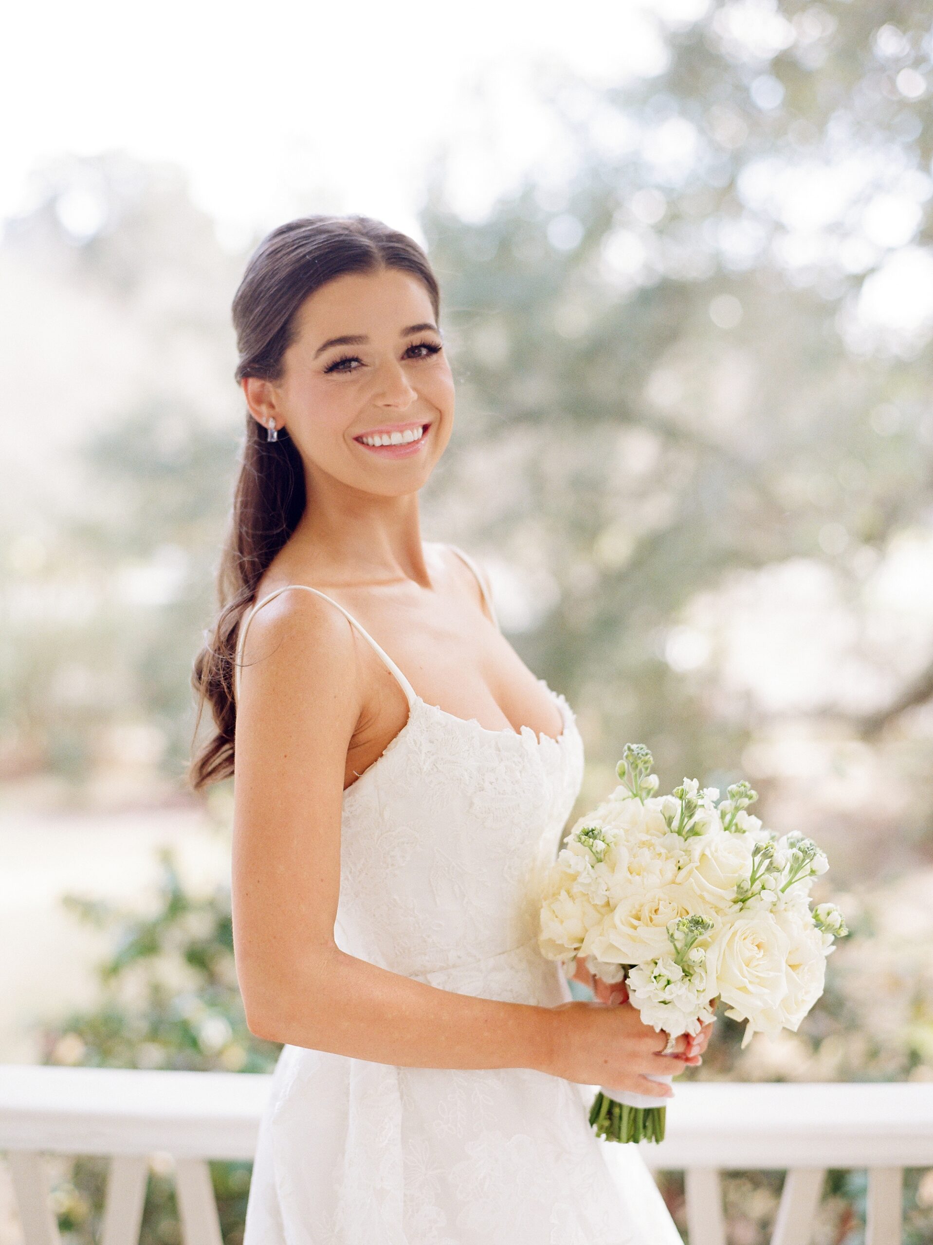 bride smiles looking over shoulder of wedding dress holding bouquet of ivory flowers 