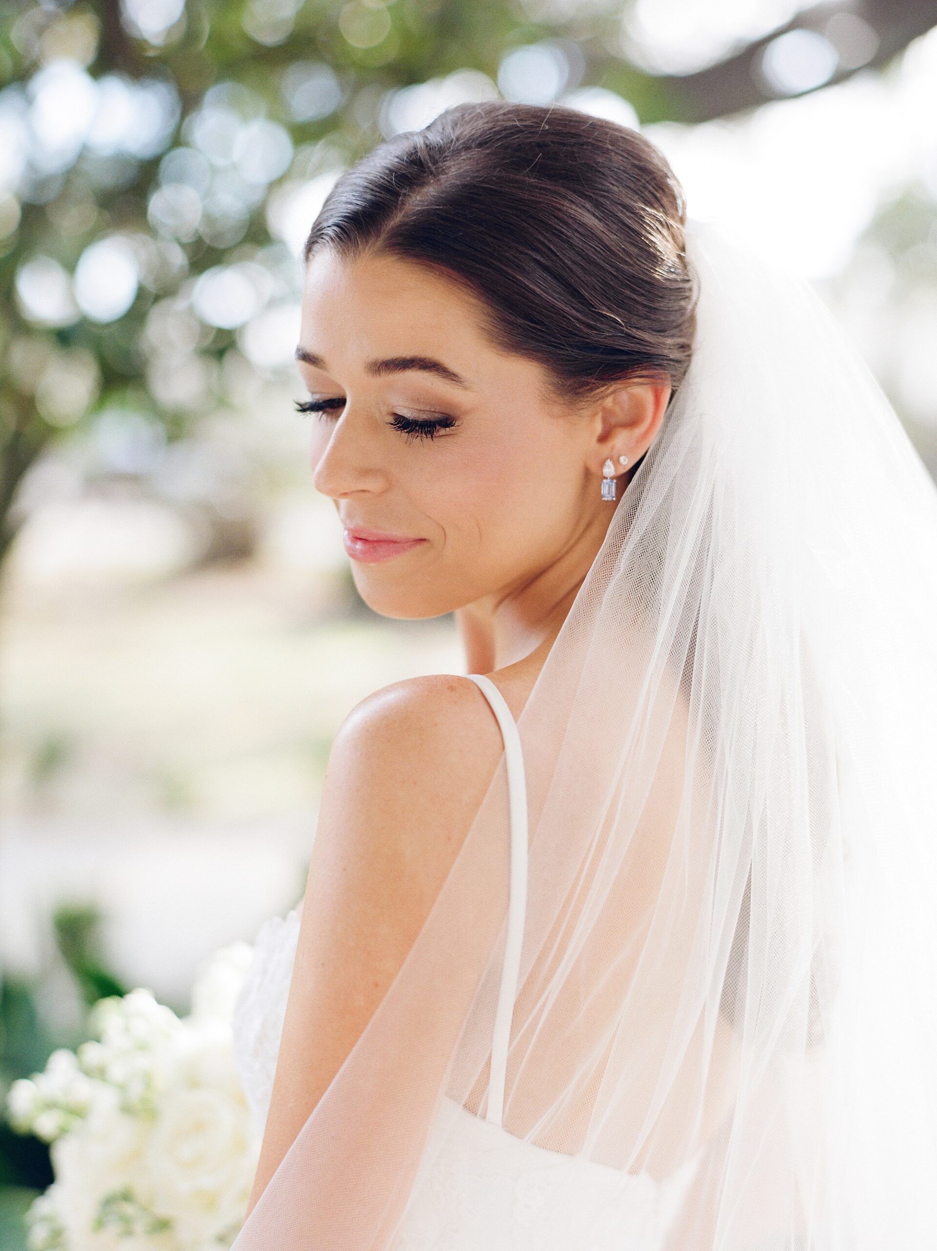 bride smiles down at shoulder looking over veil 