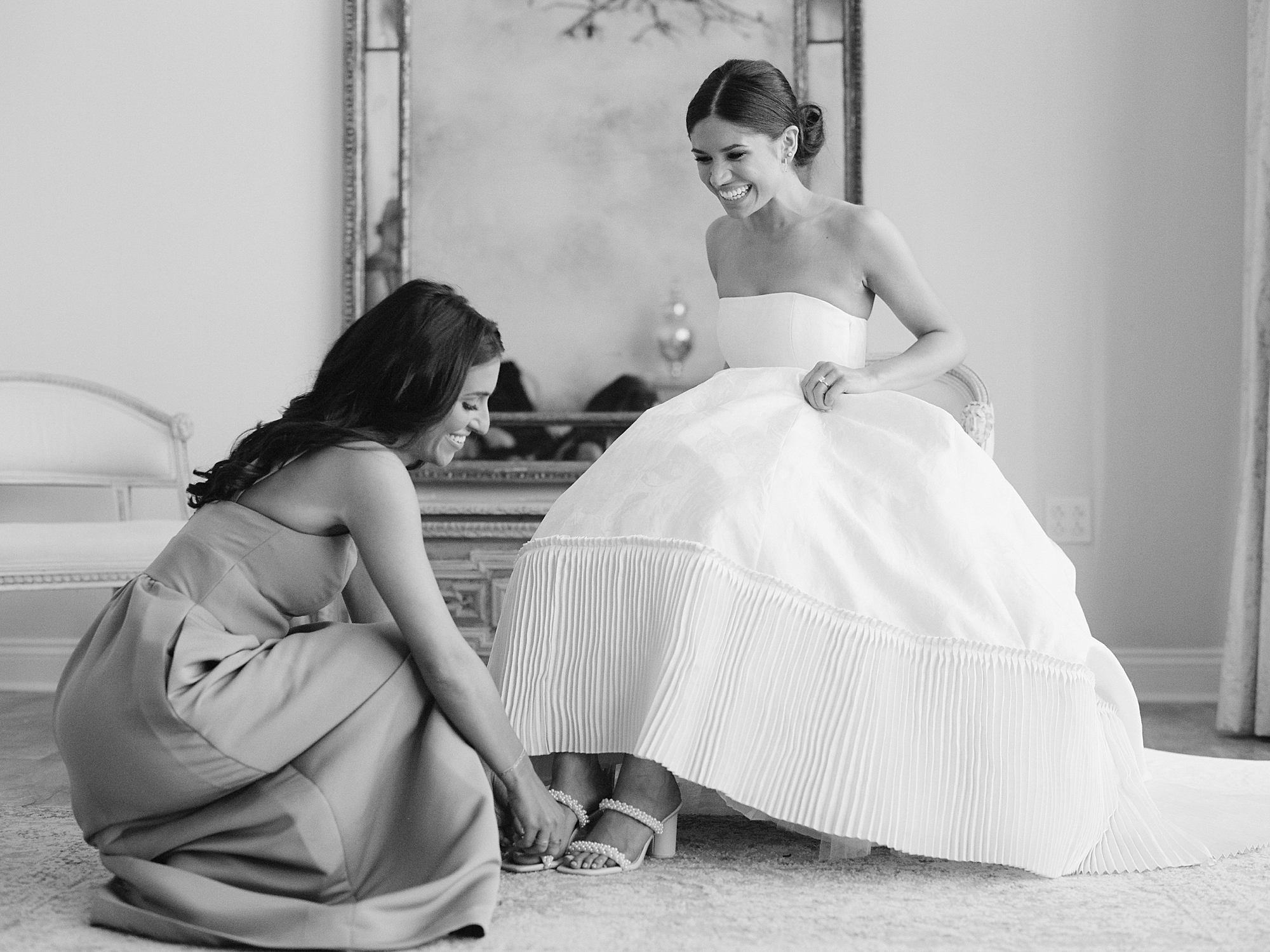 bridesmaid helps bride with shoes under skirt of ballroom gown 