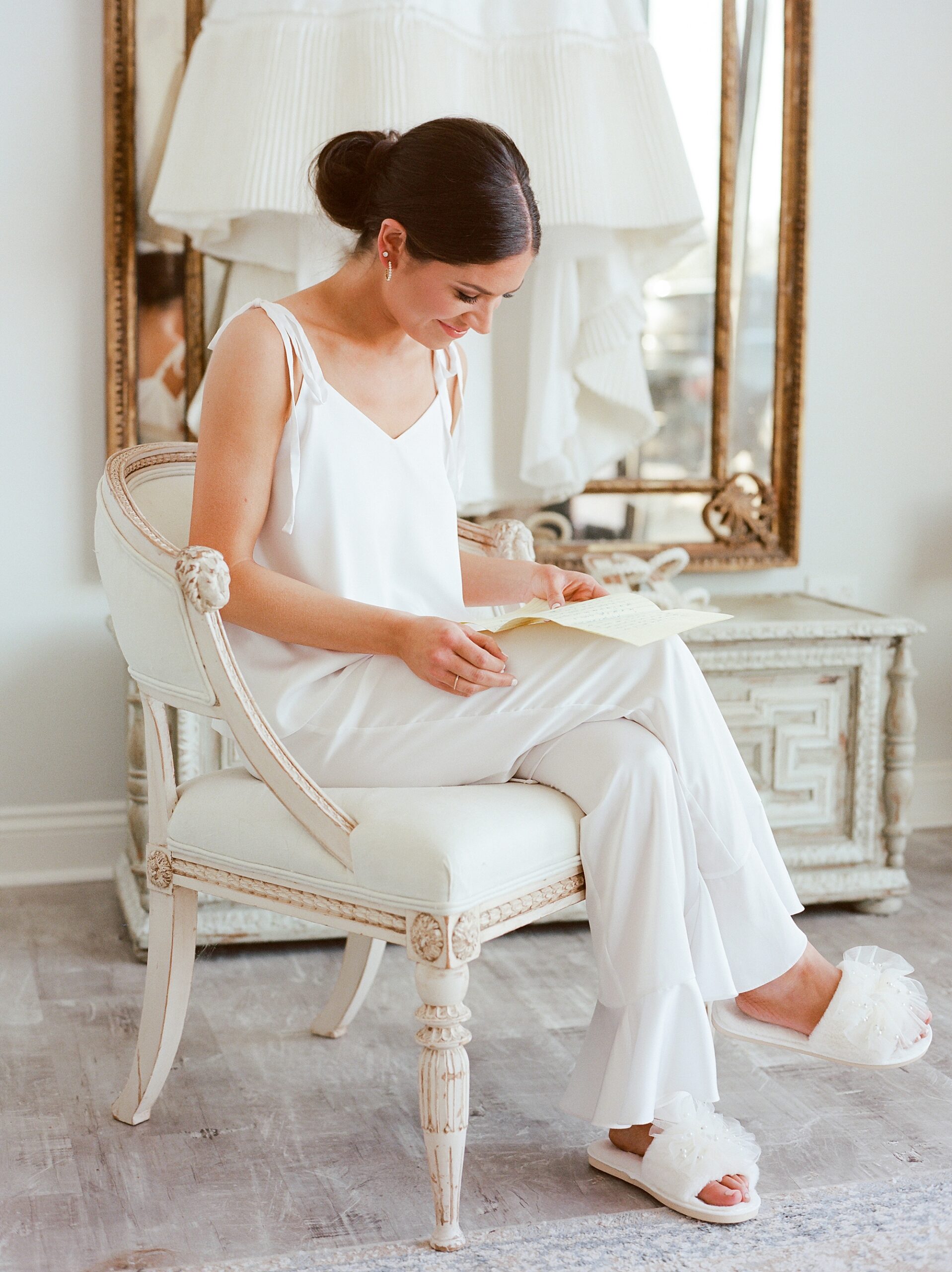 bride reads letter sitting in white pajamas with slippers 