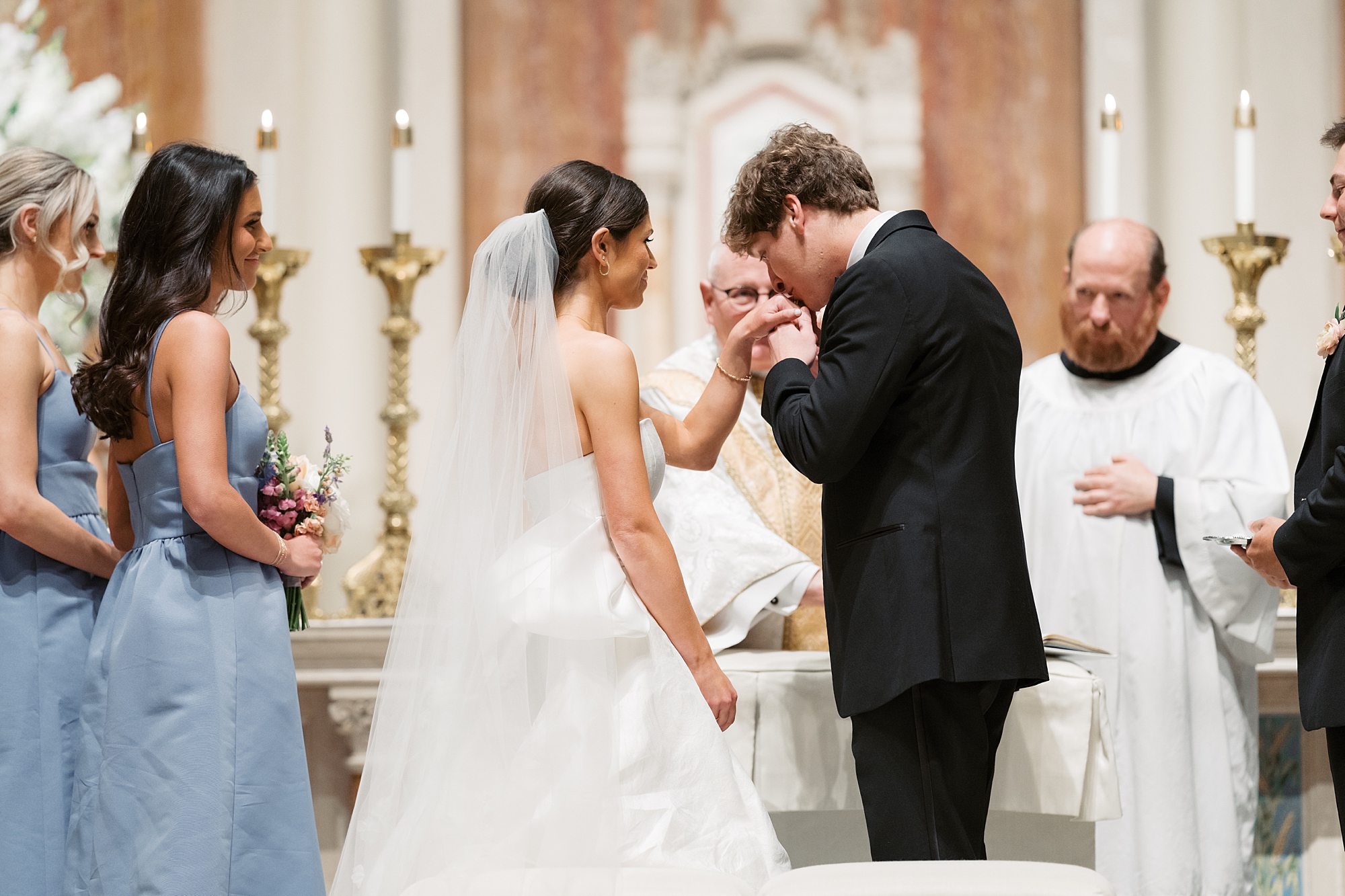 groom kisses bride's hand during wedding ceremony at St. John Cathedral