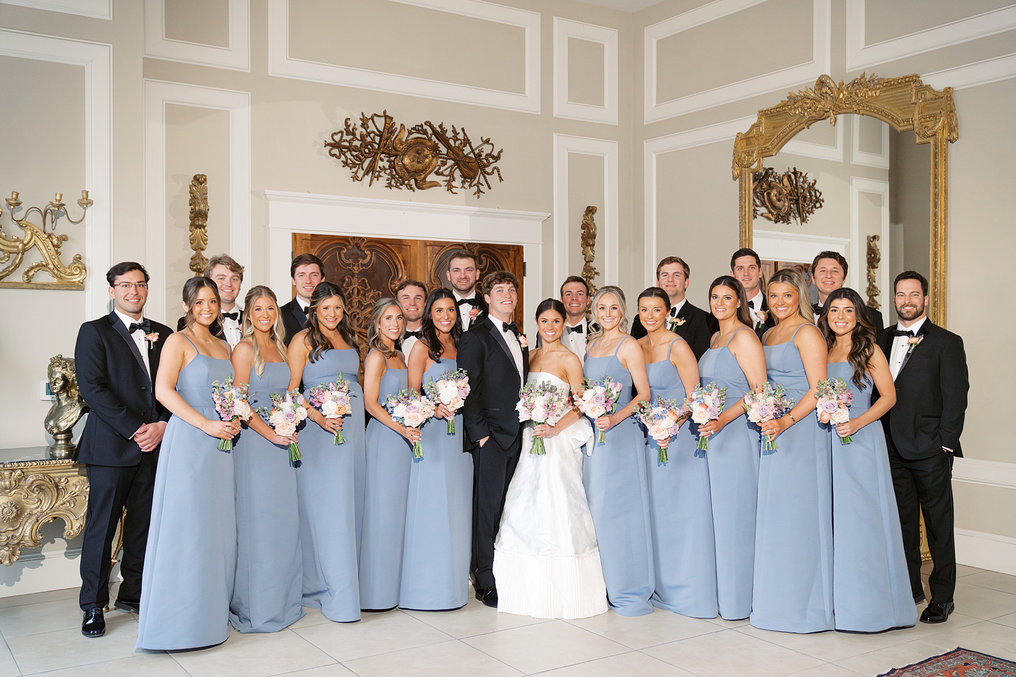 newlyweds pose with wedding party in blue dresses and black suits 